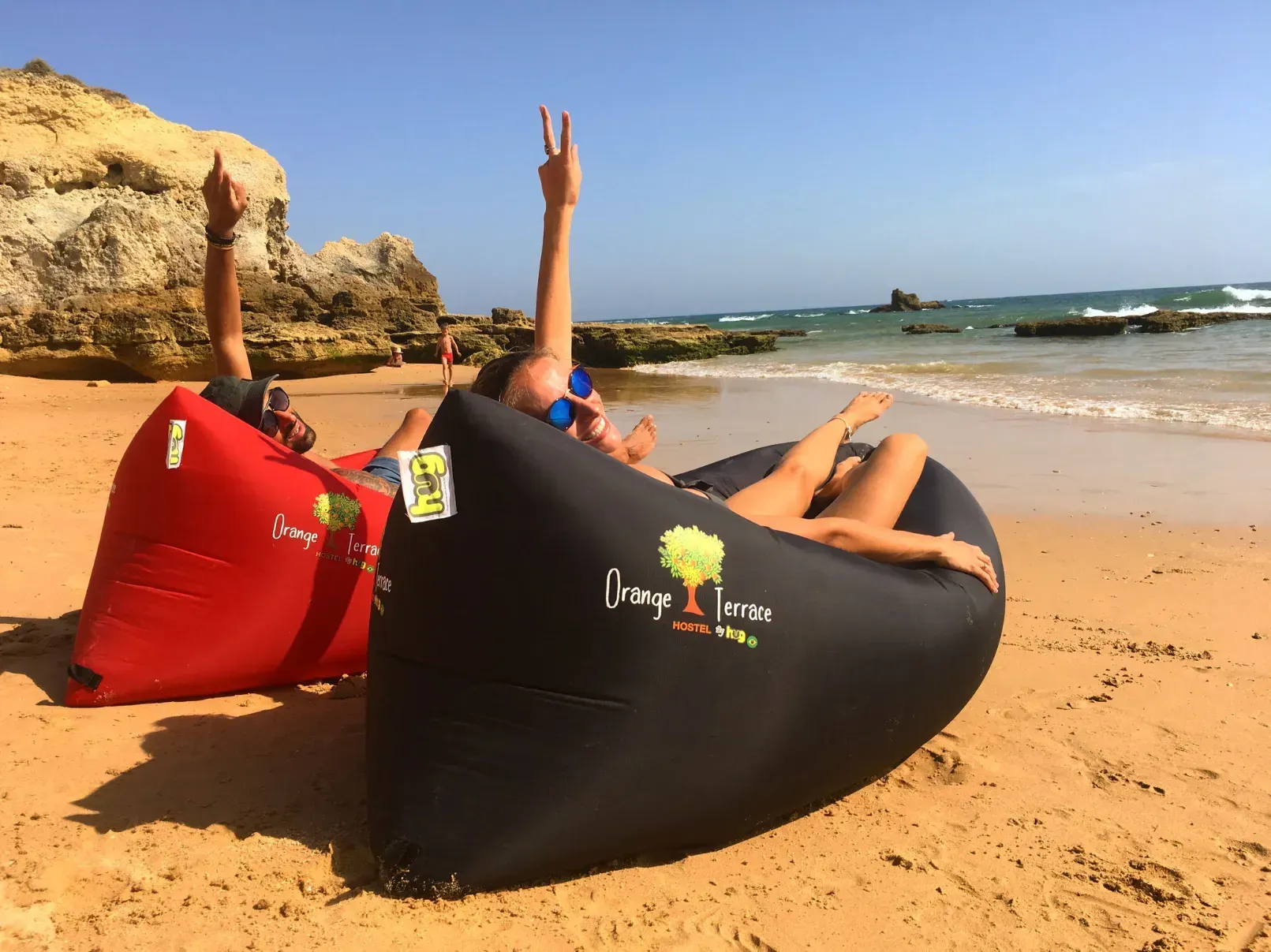 a group of people are laying on a beach in a bag that says Orange Terrace Hostel