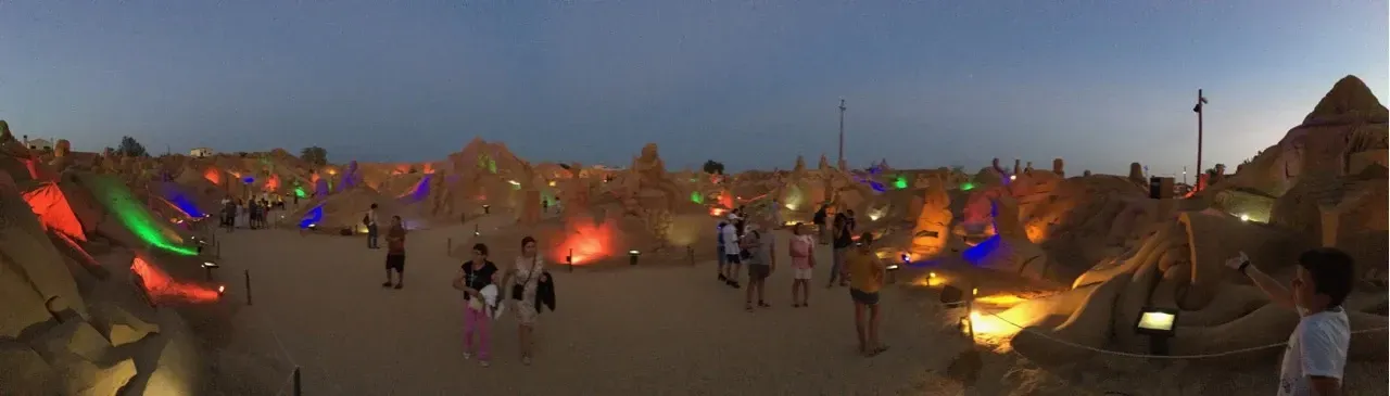 a picture of a group of people walking in the beach with Sand sculptures