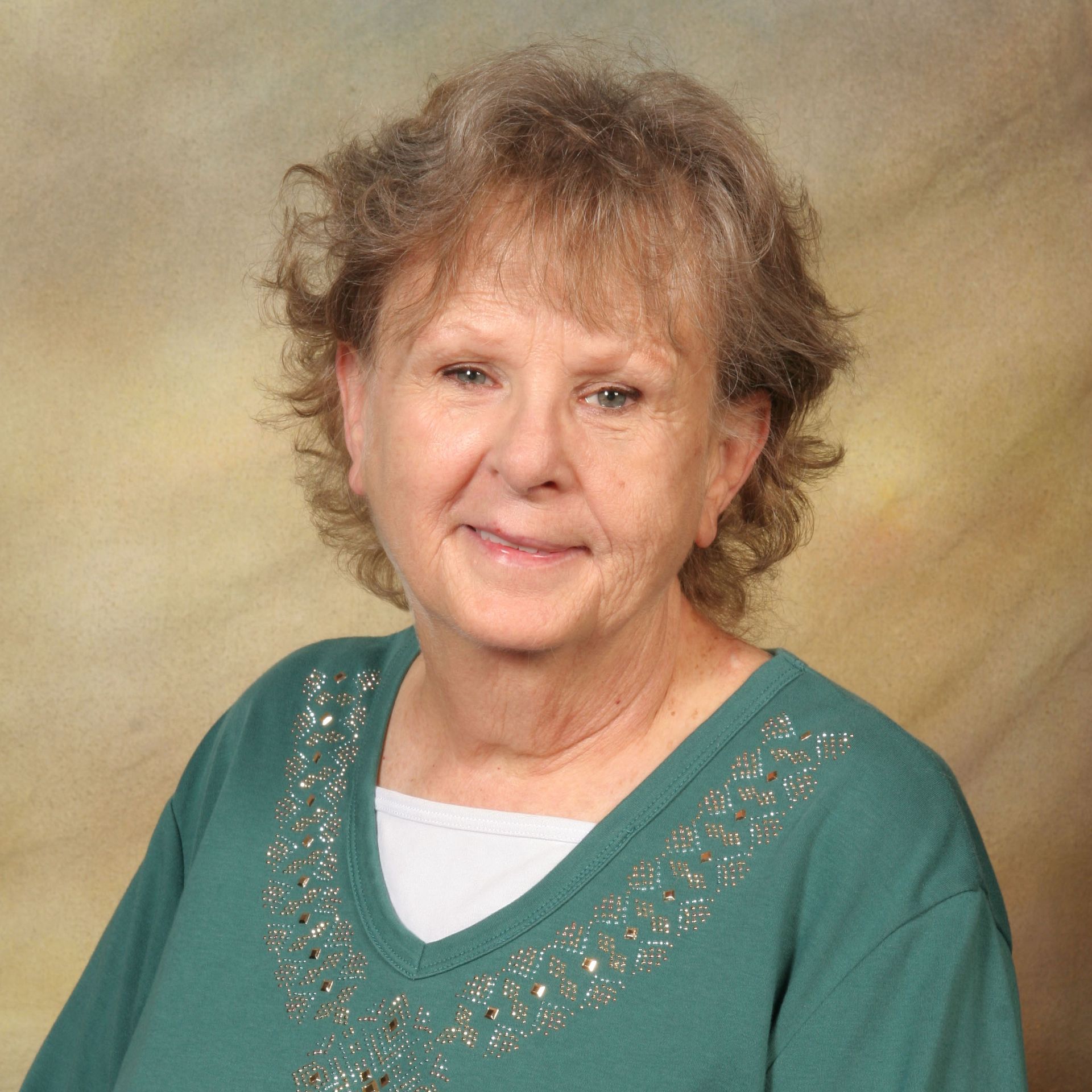 Portrait of a smiling woman in a teal top against a soft studio backdrop
