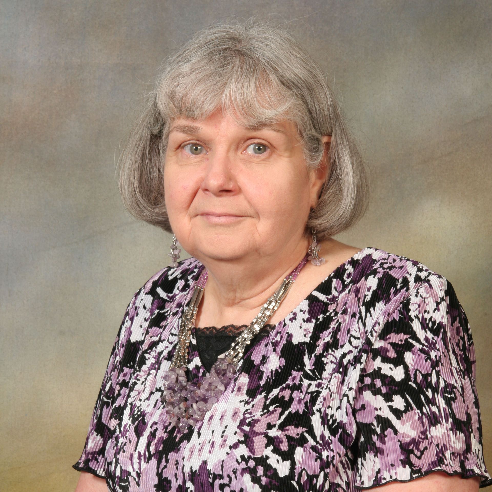 Portrait of a woman with gray hair in a pink and black patterned blouse against a neutral backdrop