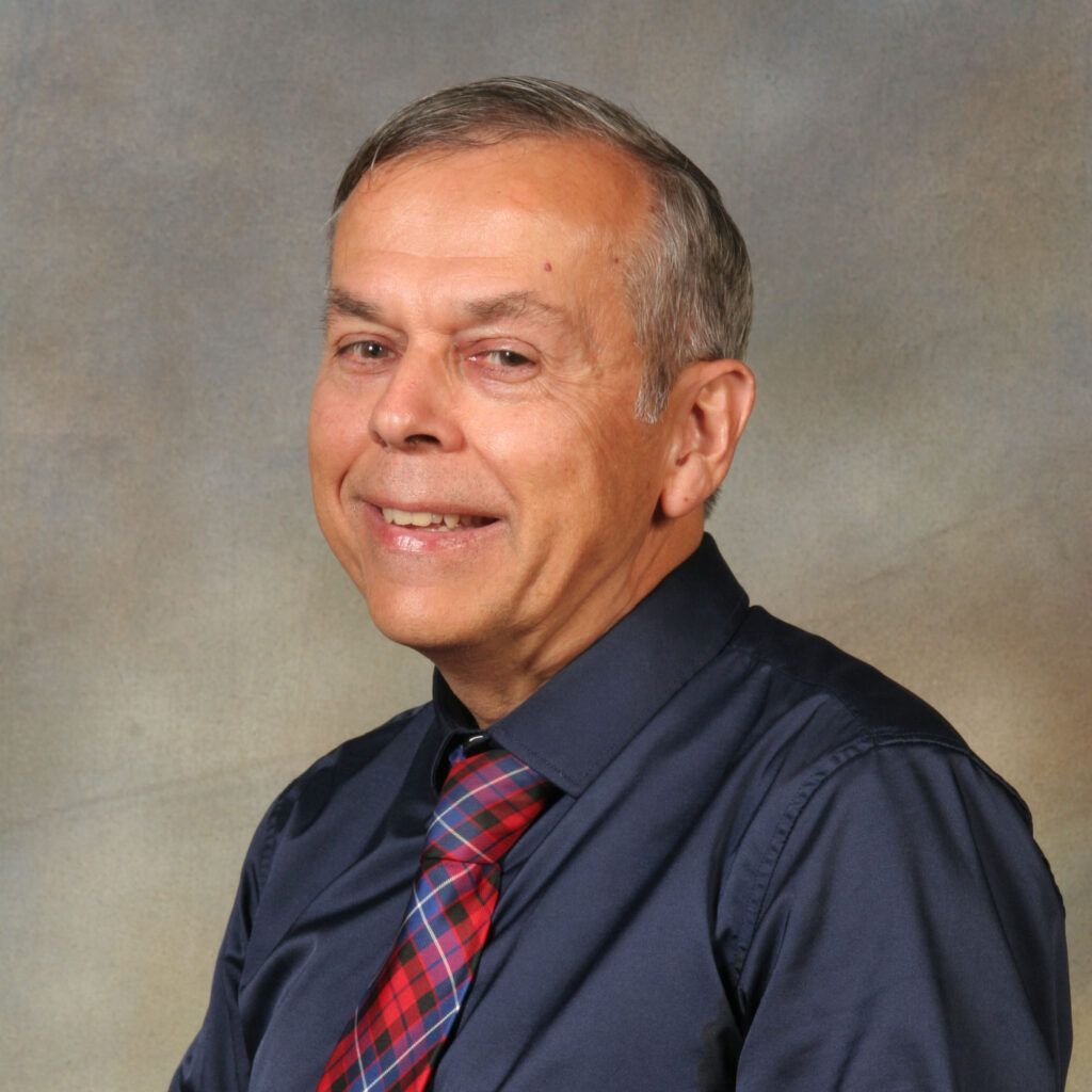 Portrait of a smiling man in a navy shirt and red plaid tie against a neutral backdrop