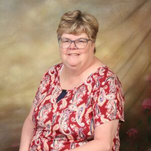 Smiling person in glasses wearing a red patterned blouse against a soft studio backdrop