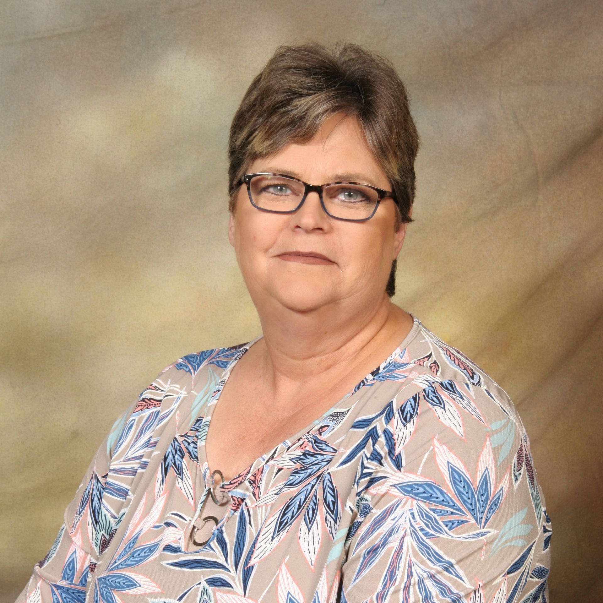 Portrait of a woman wearing glasses and a blue floral blouse against a neutral studio backdrop