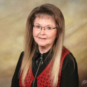 Portrait of a woman with glasses in a black top and red vest against a soft studio backdrop
