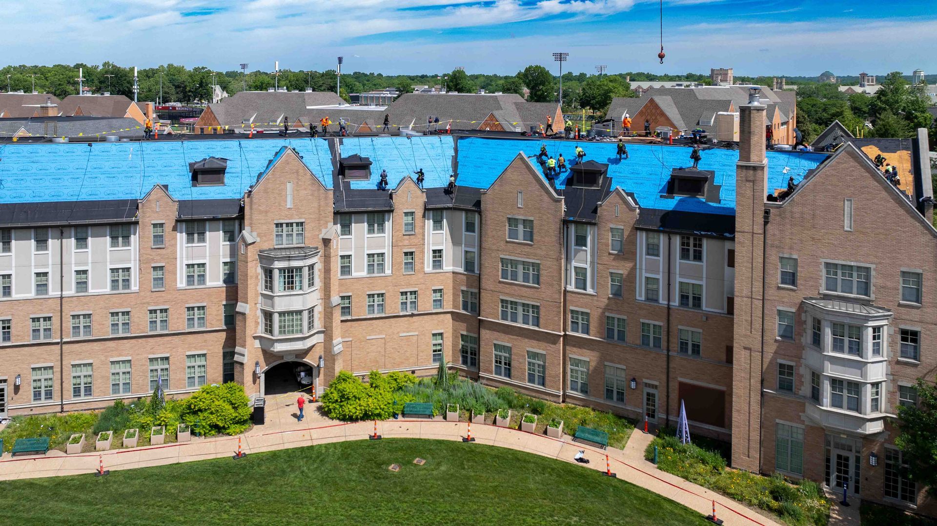 Curved tan apartment building with blue roofs, arched entryway, and green lawn under a blue sky.