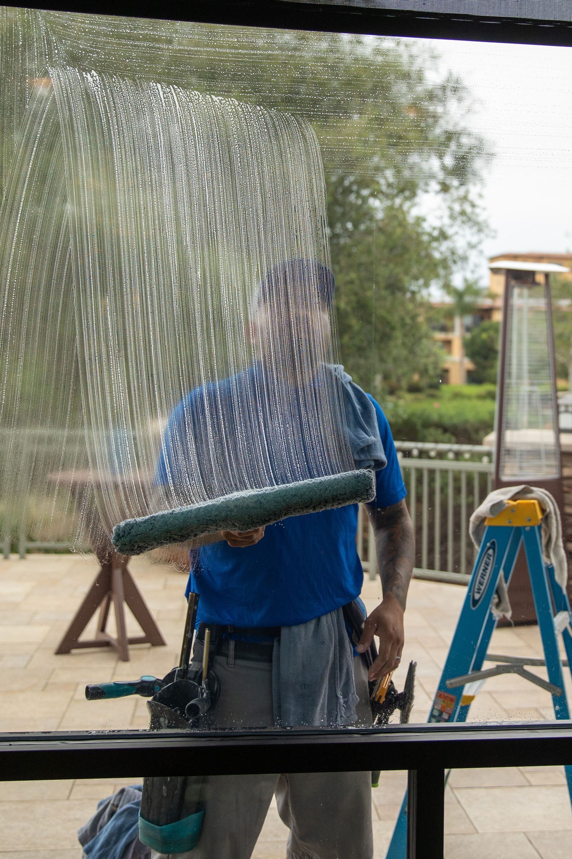 Person holding a hose sprays water at a window, creating a sheet of droplets outside.