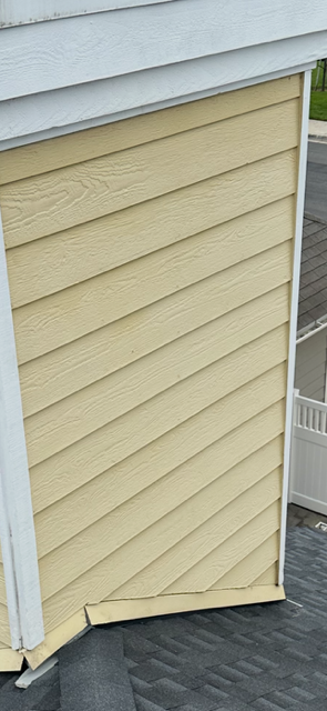 Person pressure-washing a house exterior beside a ladder and windows