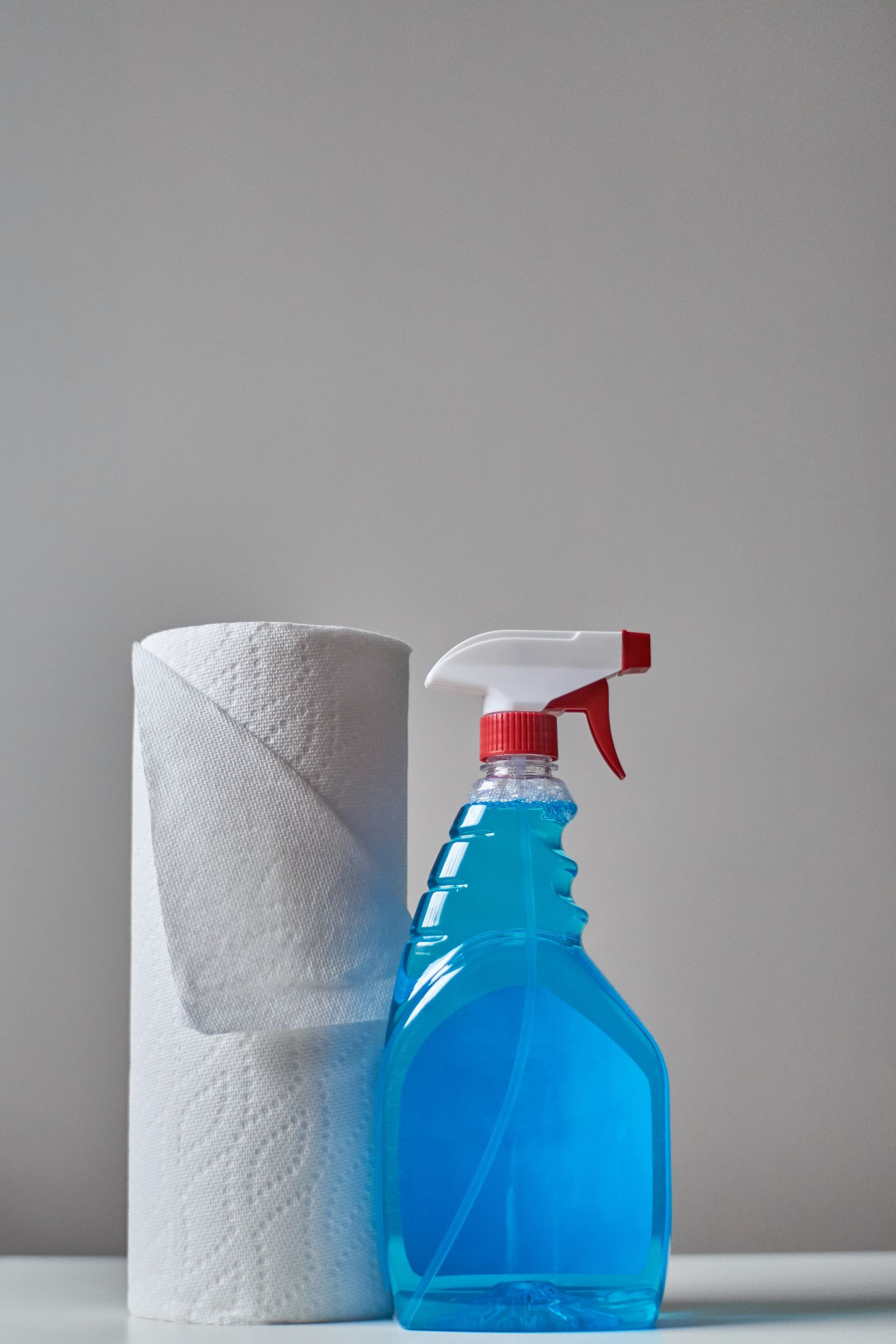 Blue spray cleaner beside a roll of white paper towels on a gray surface
