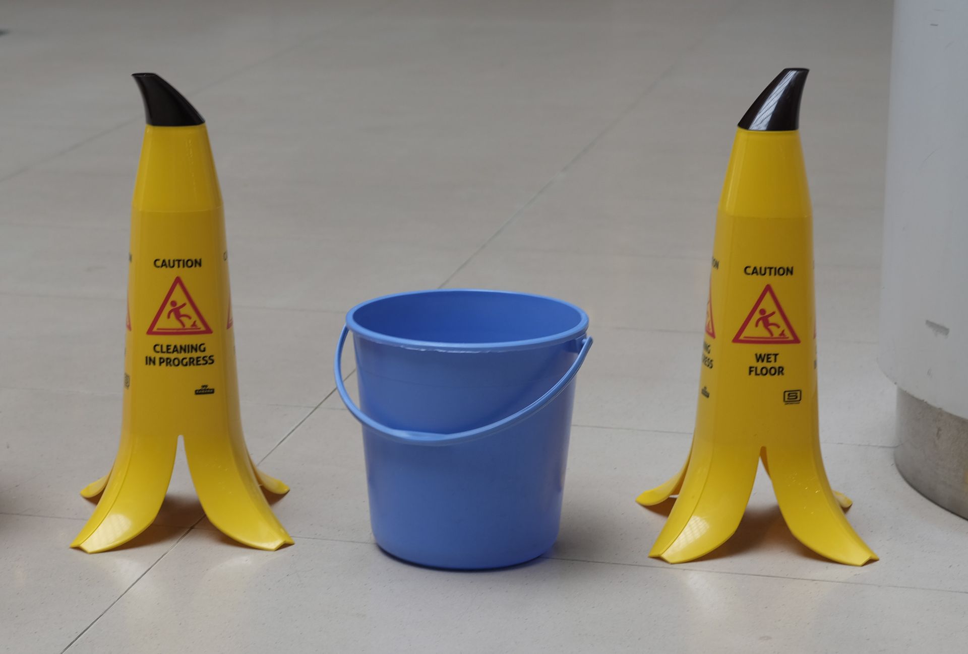 Blue bucket between two yellow caution cones on a floor