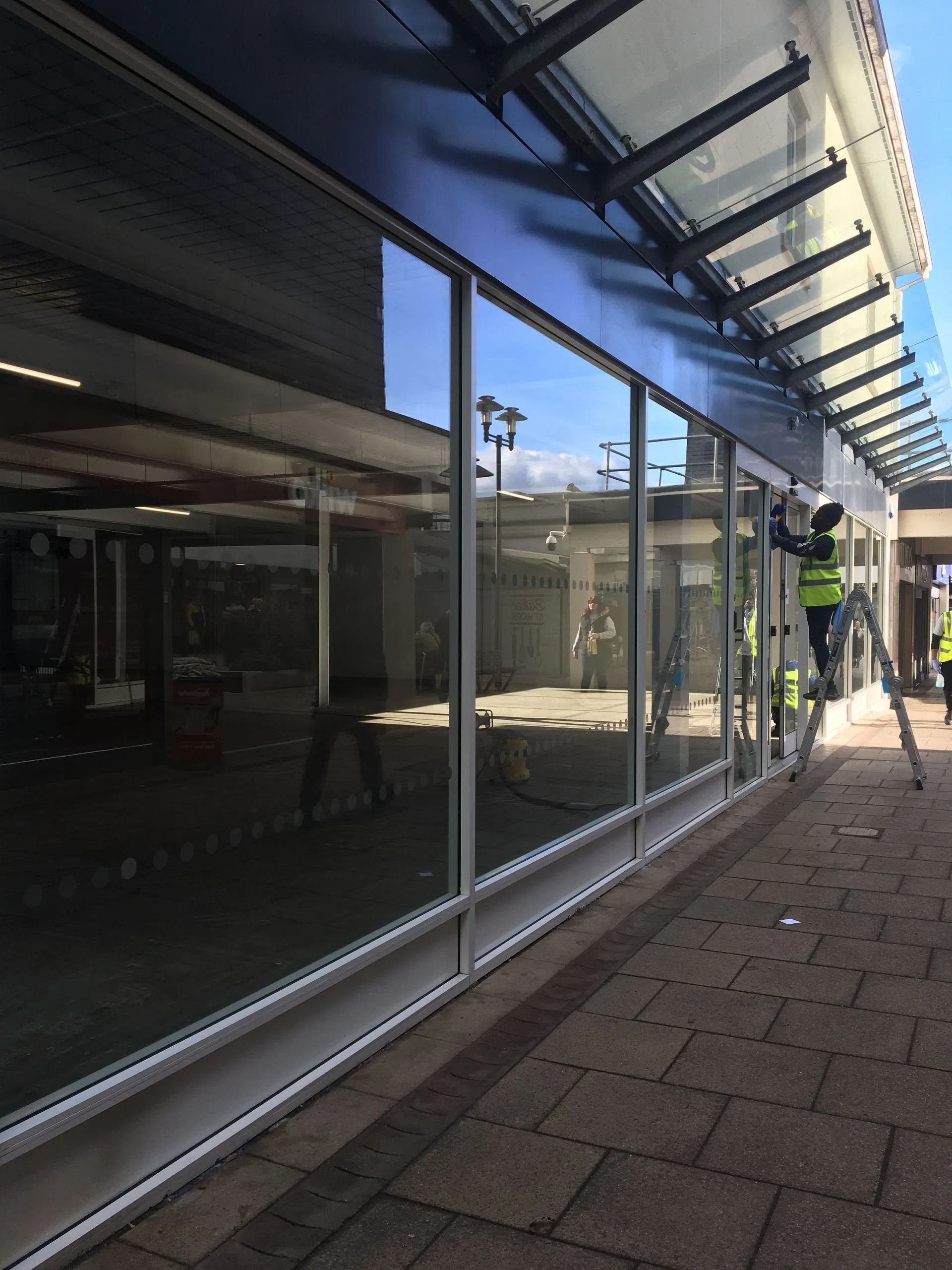 Glass storefront with reflections beside a brick walkway and blue awning on a sunny day