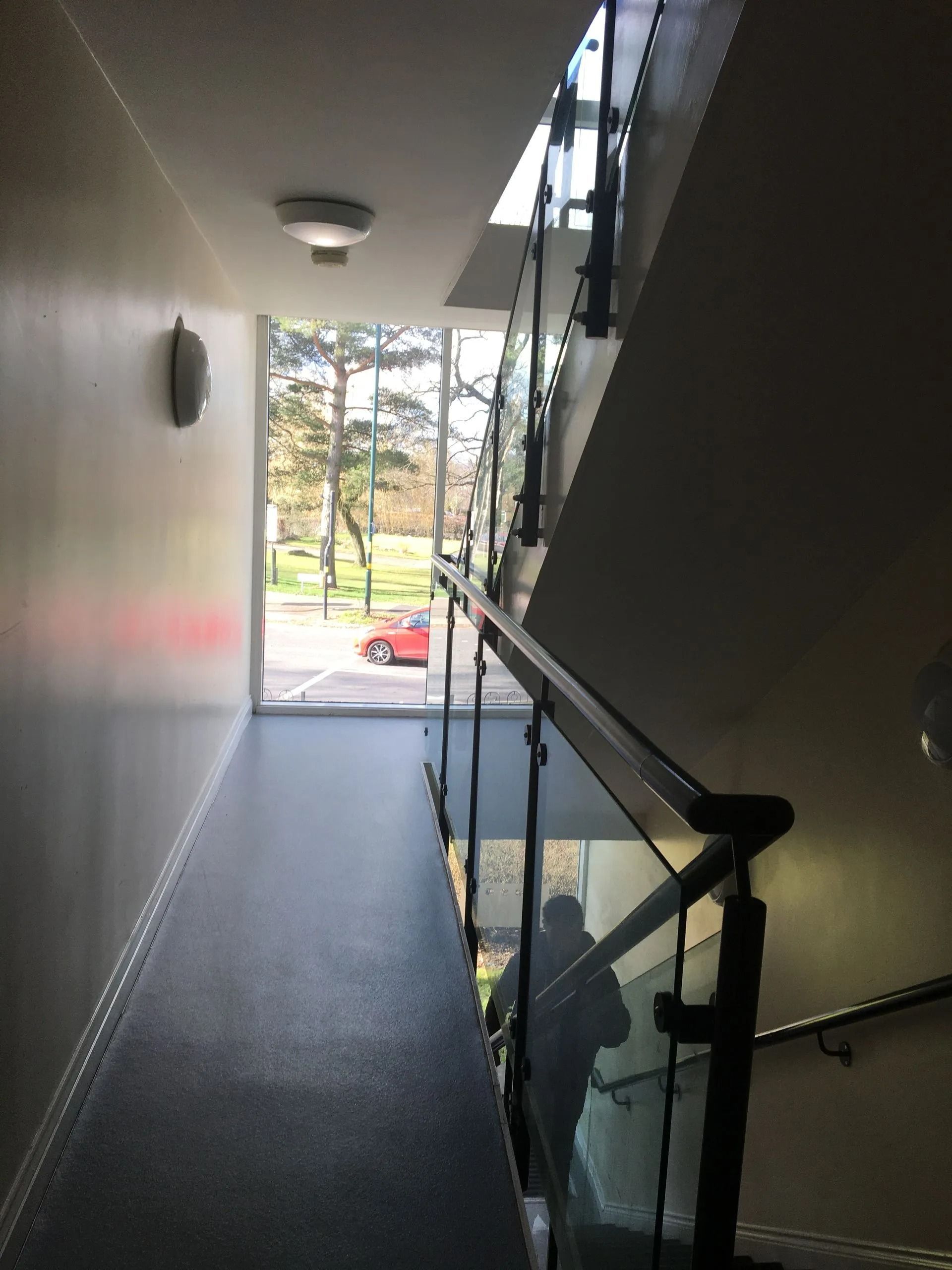 Indoor apartment hallway with stairs and glass railing, looking out to a bright exterior courtyard