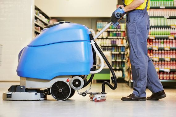 Floor scrubber machine cleaning store aisle beside a worker in a supermarket aisle