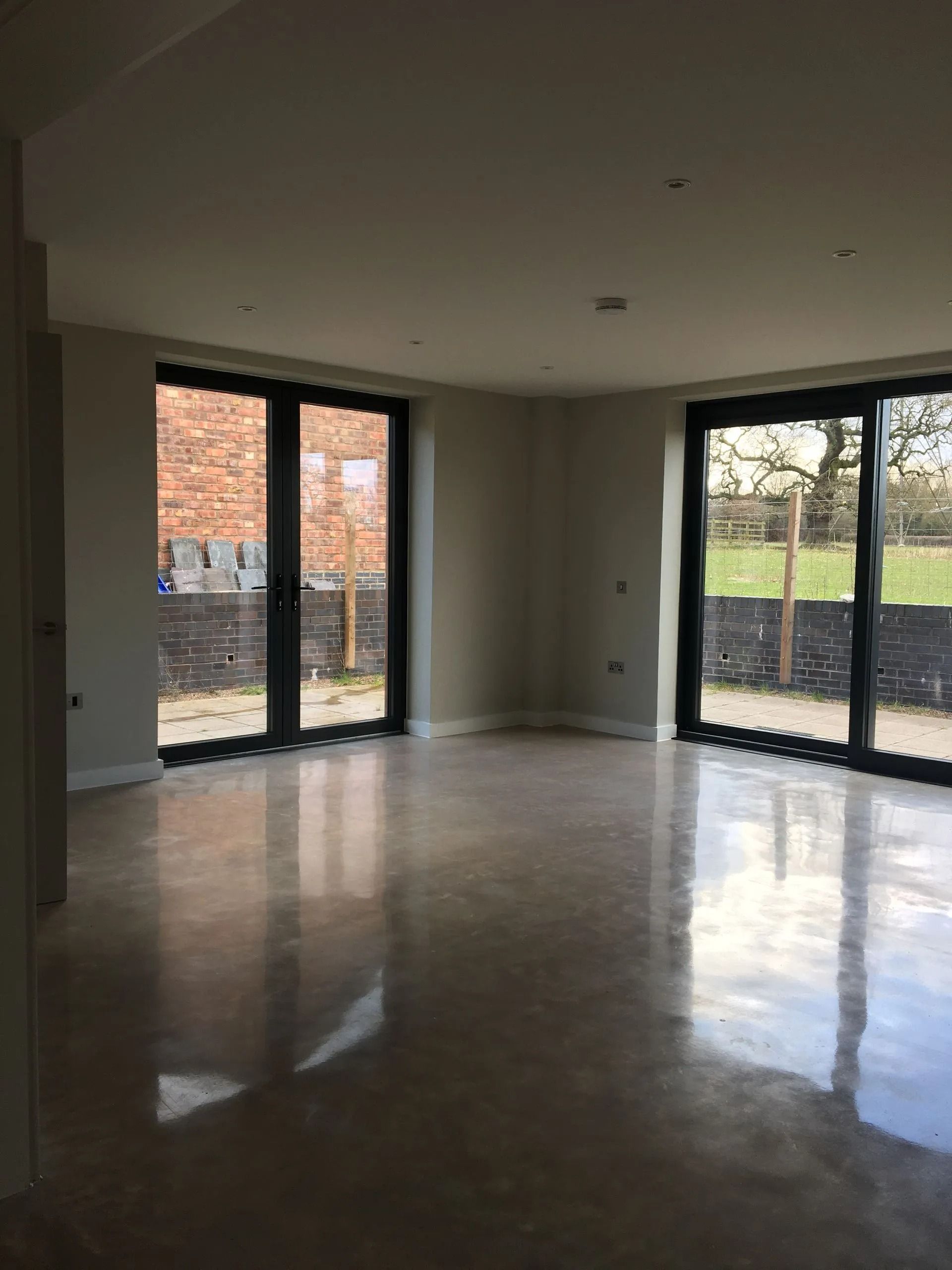 Empty modern room with large glass doors, polished floor, and daylight streaming in