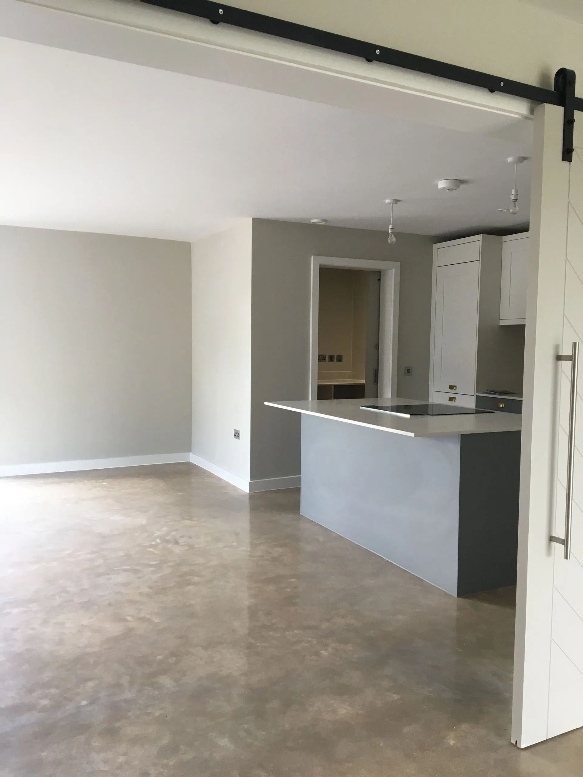 Empty unfurnished room with gray walls, concrete floor, and a small kitchen counter