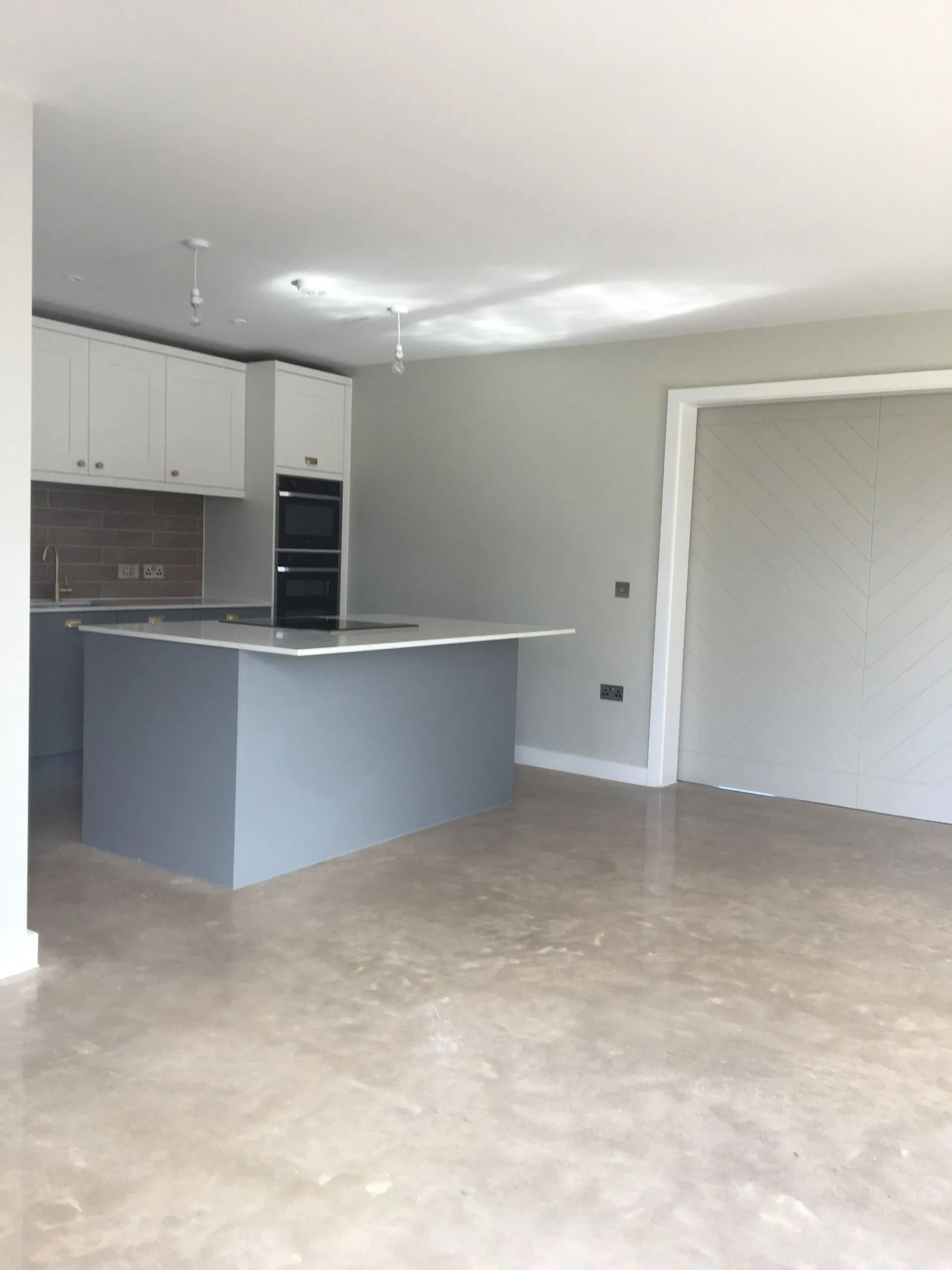 Empty modern kitchen and living area with gray island, white cabinets, and tiled floor.
