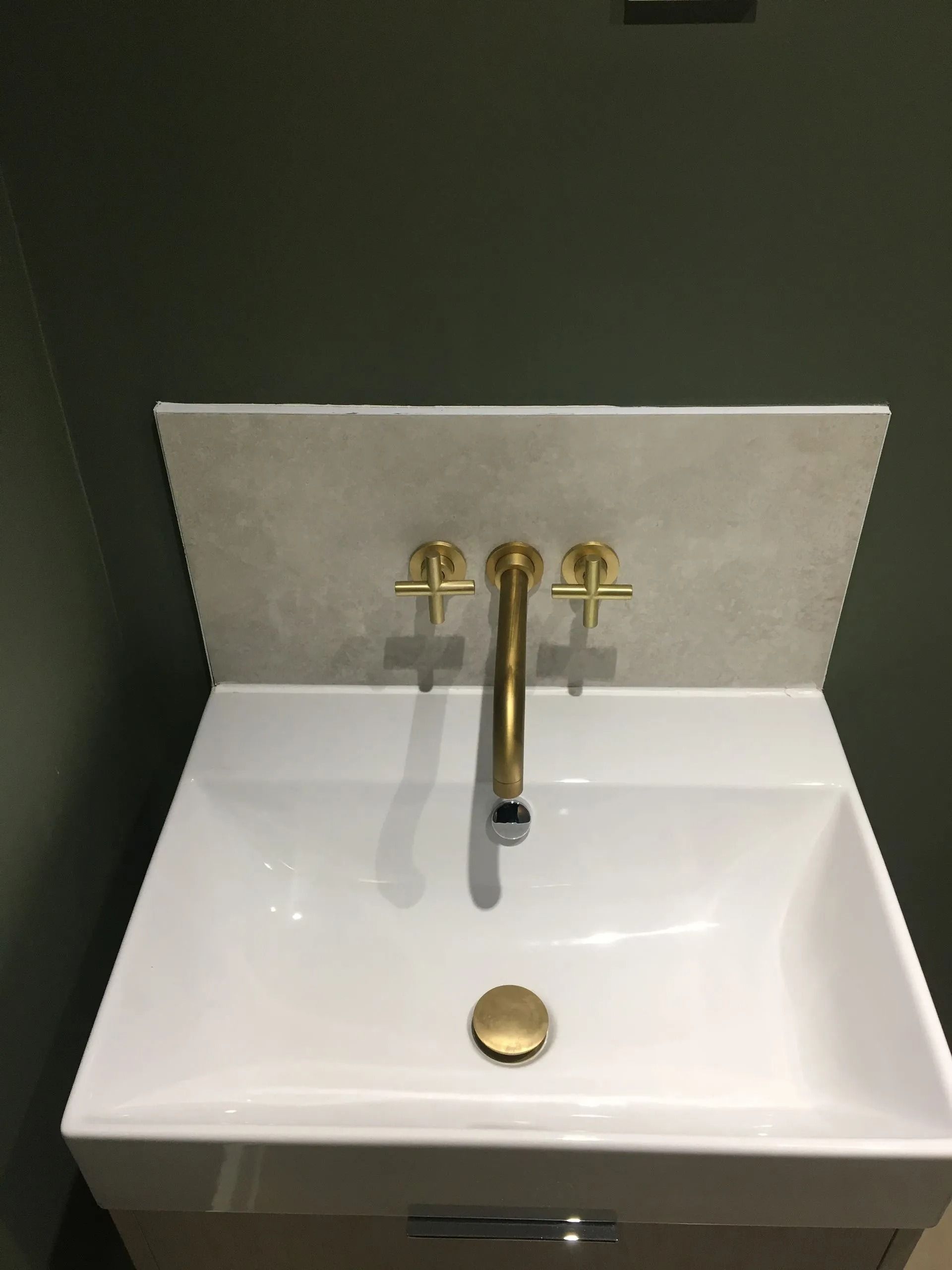 White sink with brass faucet and drain in a small dark-walled bathroom.
