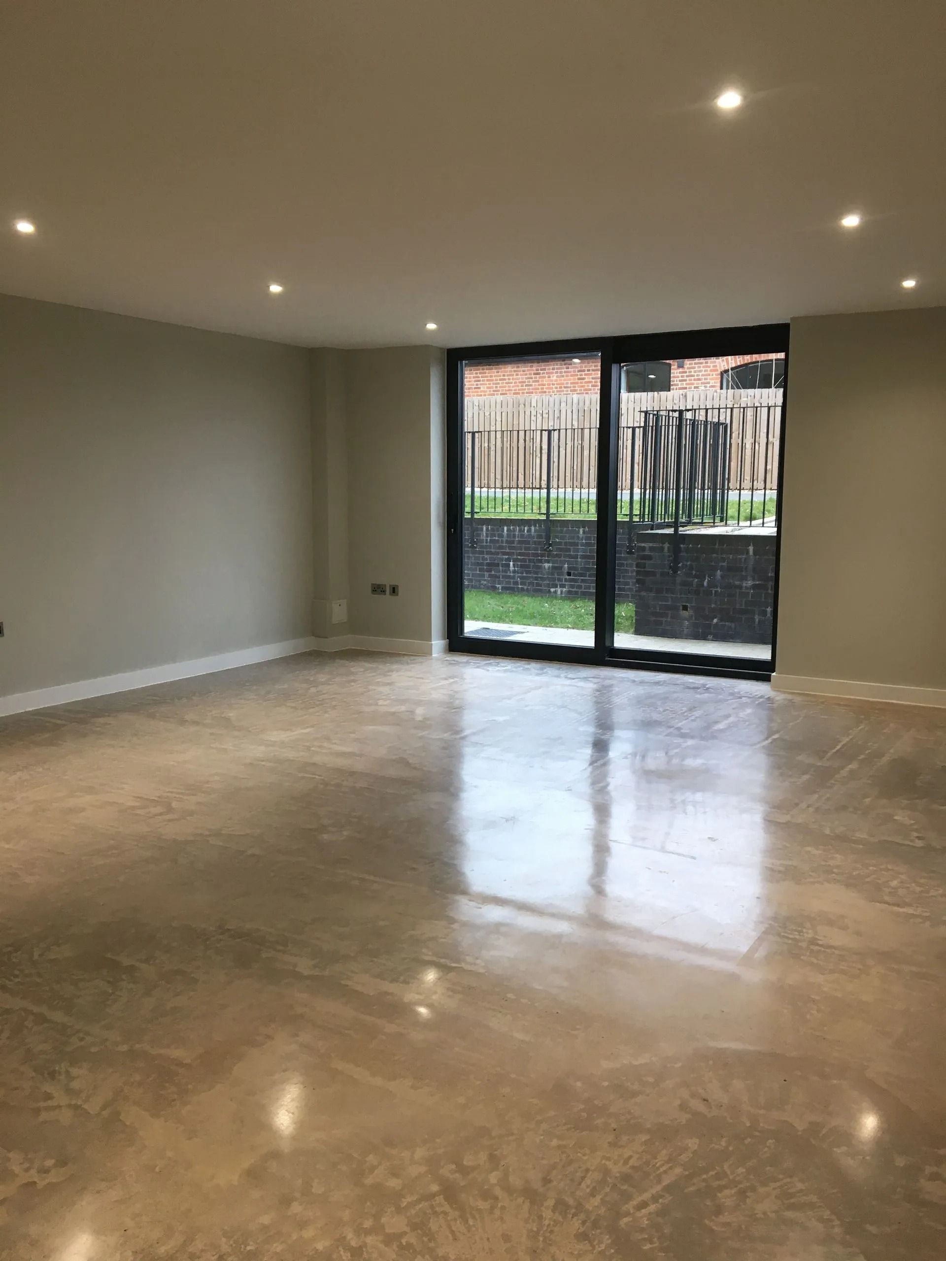 Empty modern room with beige tile floor, recessed lights, and glass doors opening to a garden.