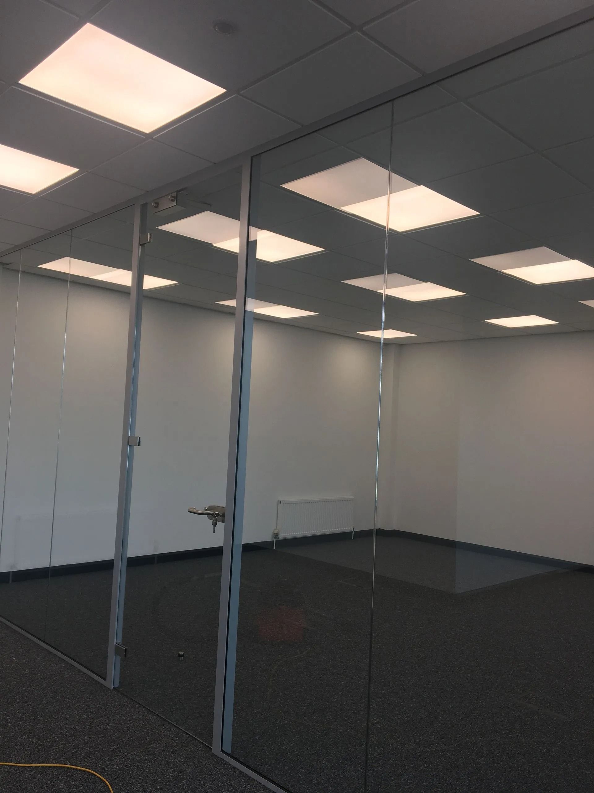 Empty office room with glass partition walls, white walls, dark carpet, and bright ceiling lights
