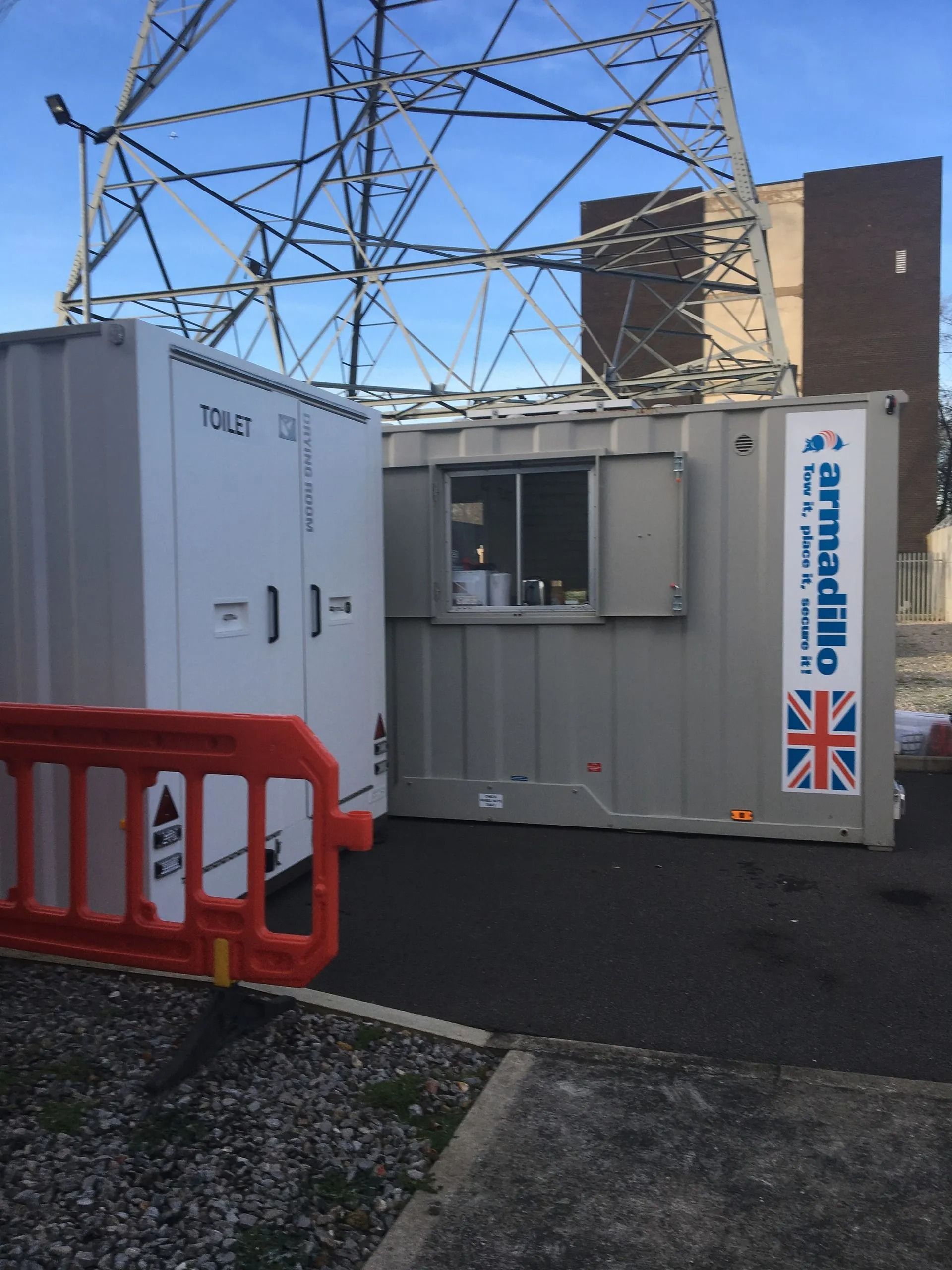 White utility container beside orange barrier and metal tower on a rooftop, with a UK flag sign.
