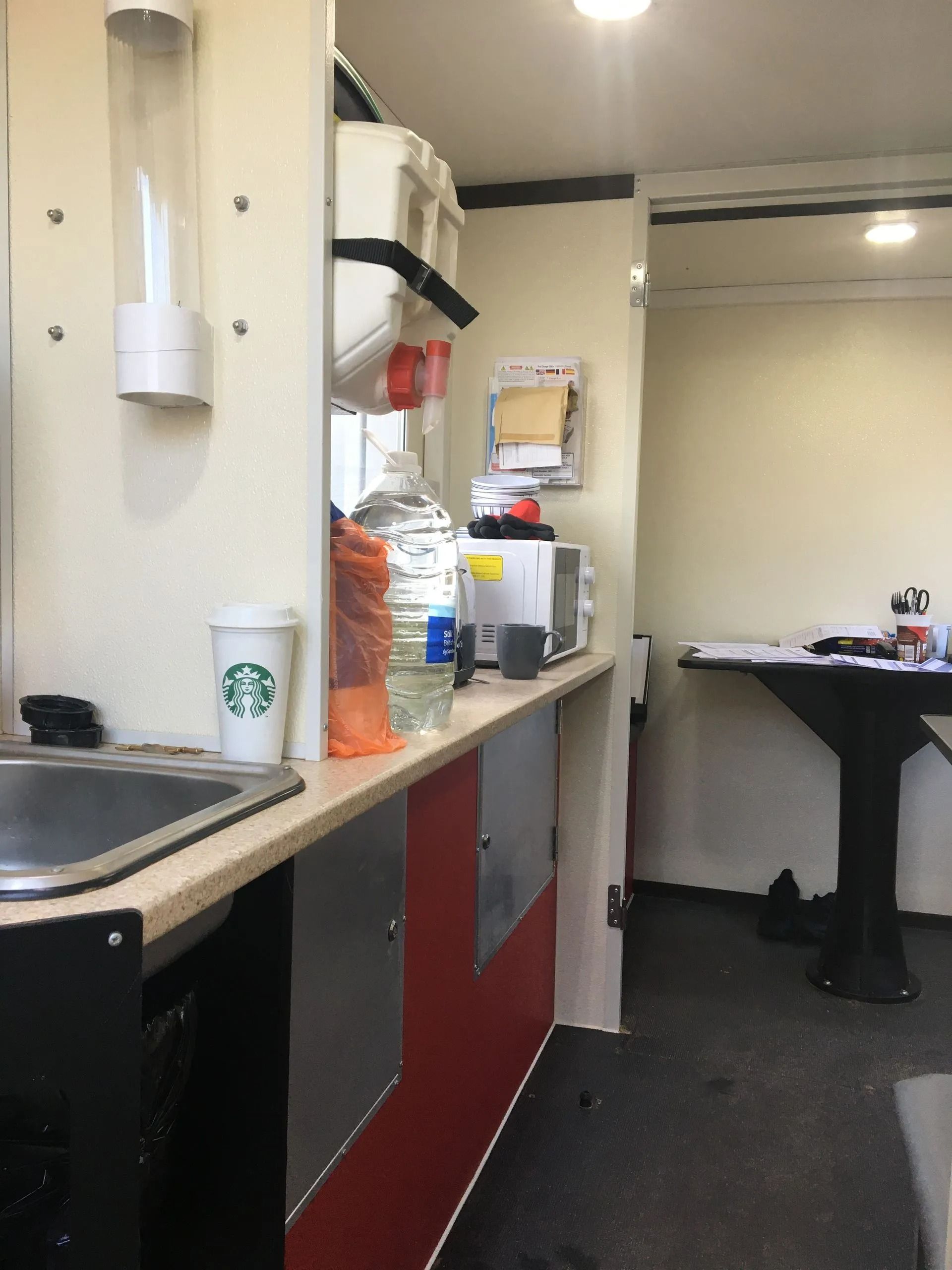 Break room with sink, coffee supplies, and a table along a narrow carpeted corridor