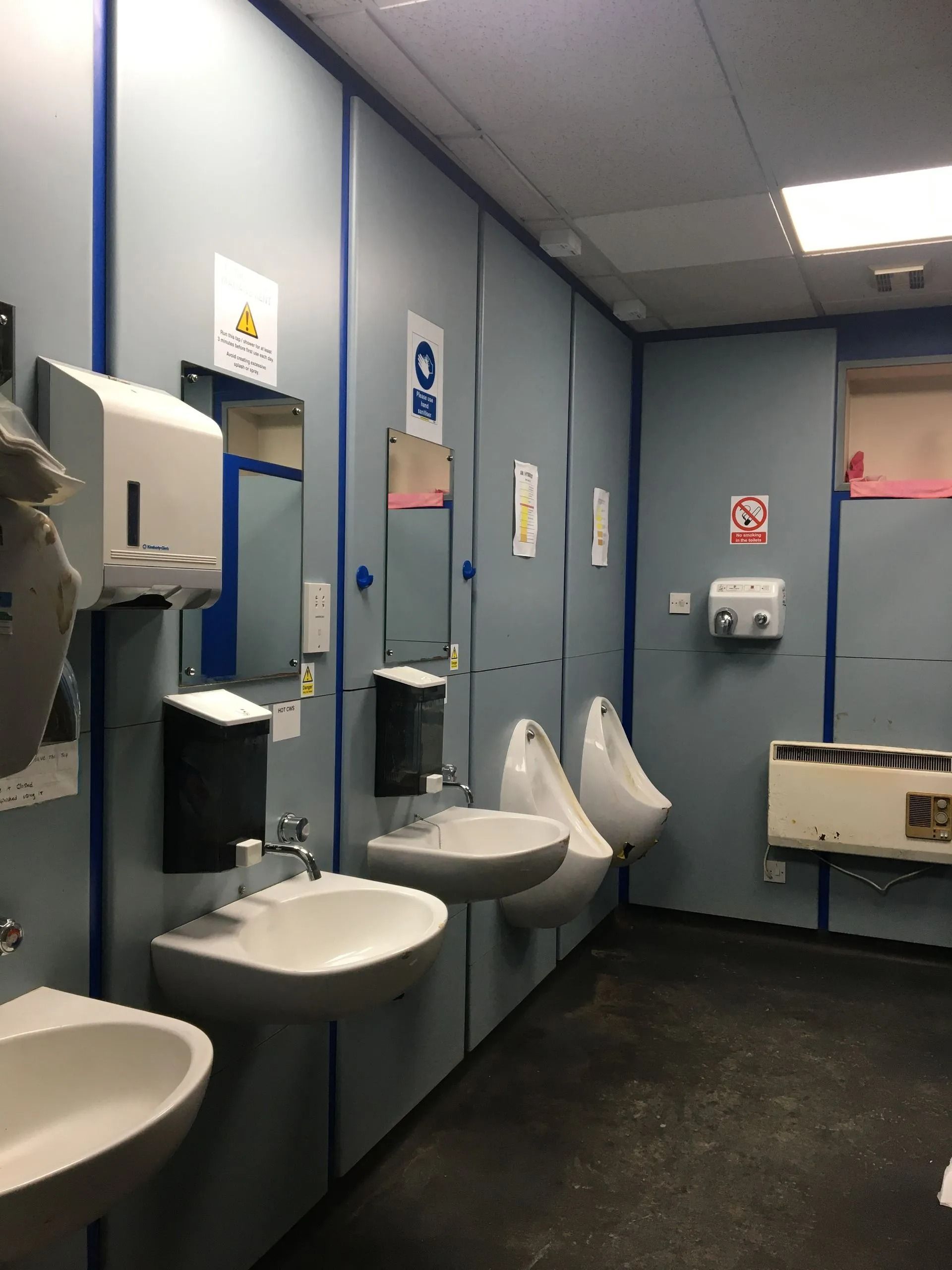 Public restroom with blue stalls, sinks, hand dryers, and a dark floor.