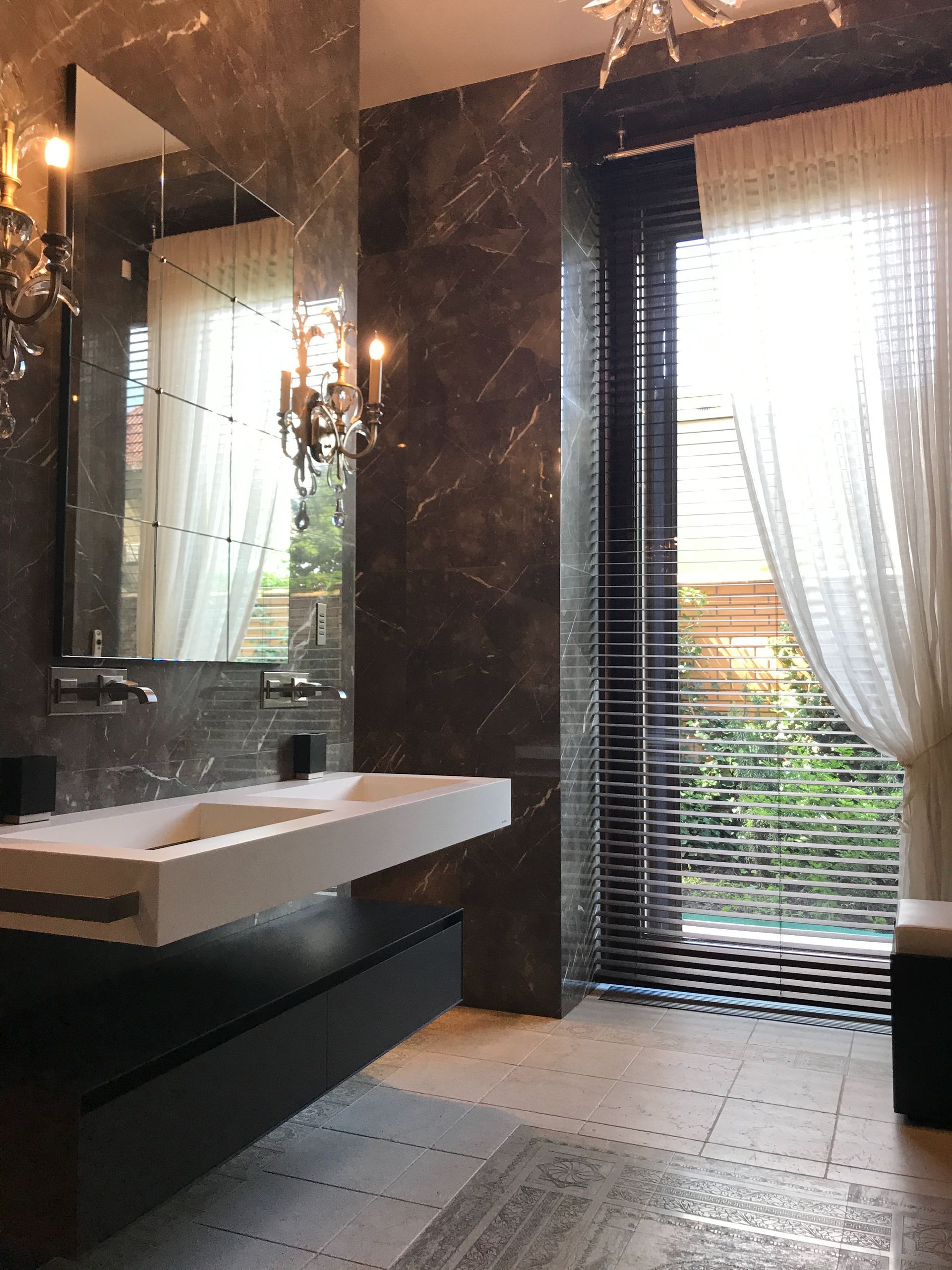 Modern bathroom with a wall-mounted sink, dark tile, mirror, and sheer curtains by a window