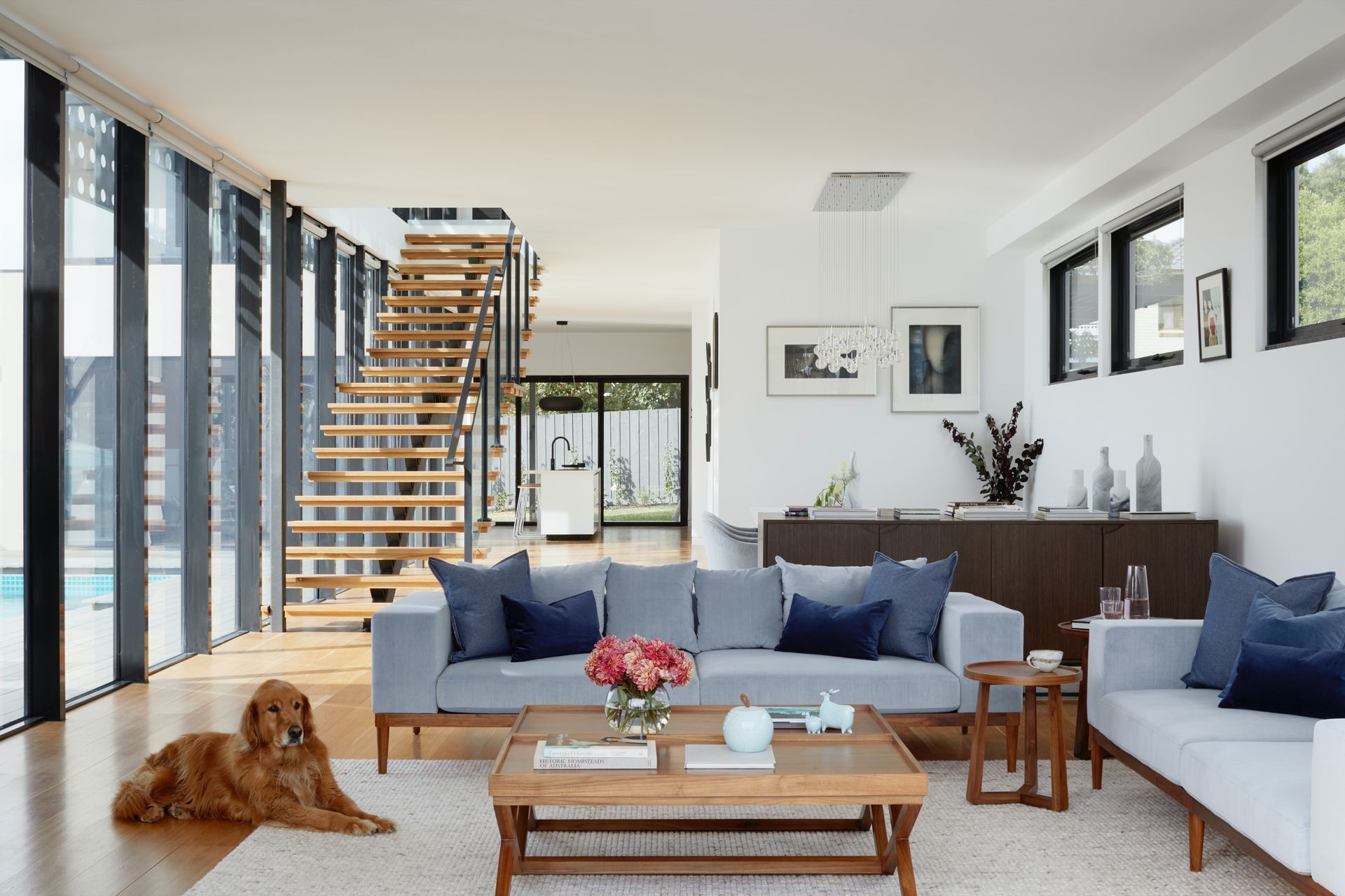 Modern living room with blue sofas, wooden staircase, and a dog lying on the floor.