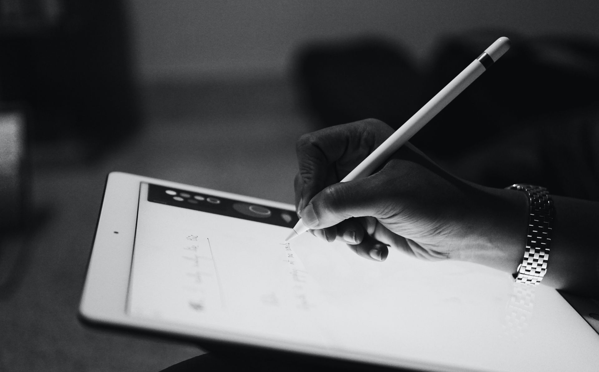 Hand holding a stylus over a tablet in a dimly lit workspace