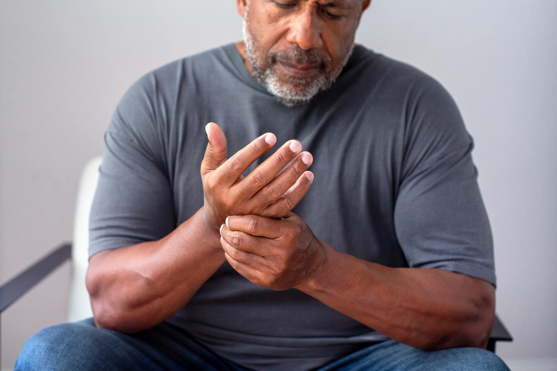 A man is sitting in a chair holding his wrist in pain.