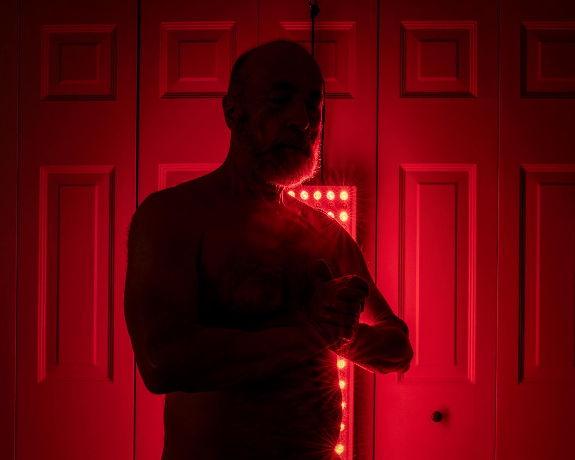 A man with a beard is standing in front of a red light.