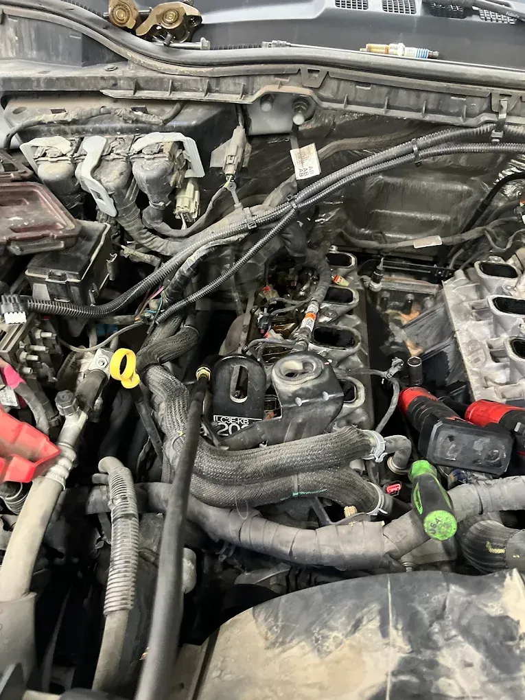 Open car engine bay with removed components, tools visible. Black engine, wires, and hoses.