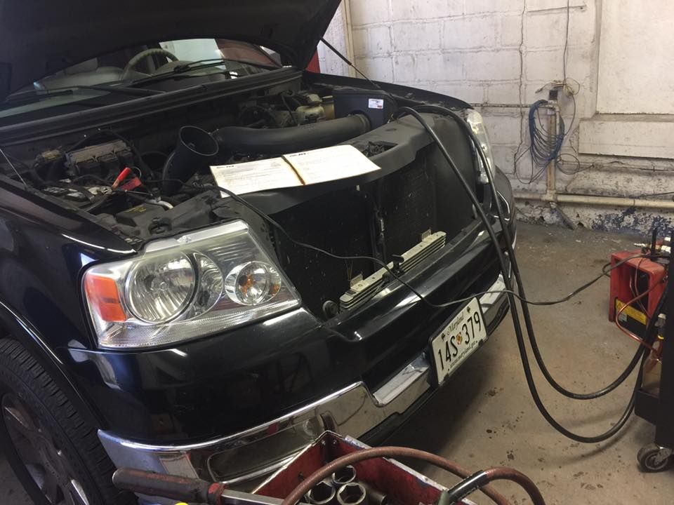 Black Ford pickup truck with its hood open in a garage, connected to diagnostic equipment.