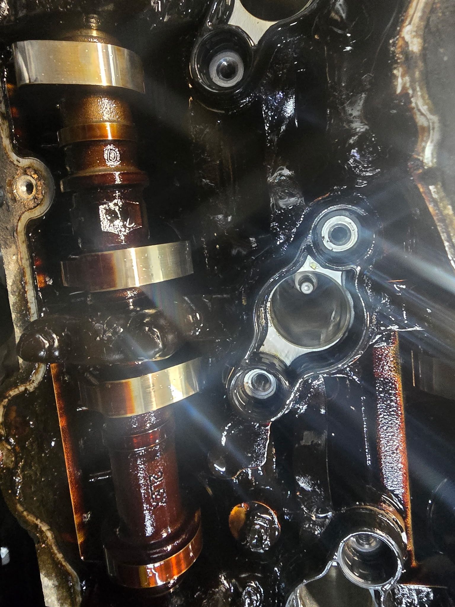 Engine components covered in oil, including a camshaft and mounting hardware.