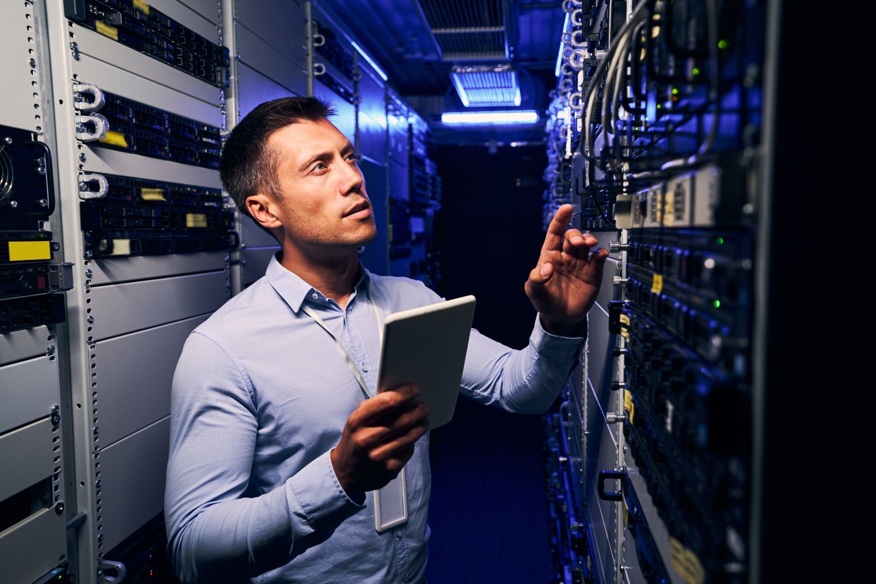 A man is looking at a tablet in a server room.