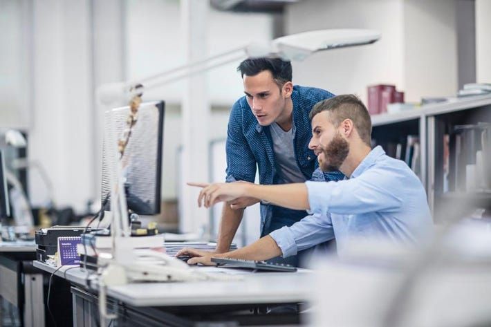 Two men are looking at a computer screen in an office.