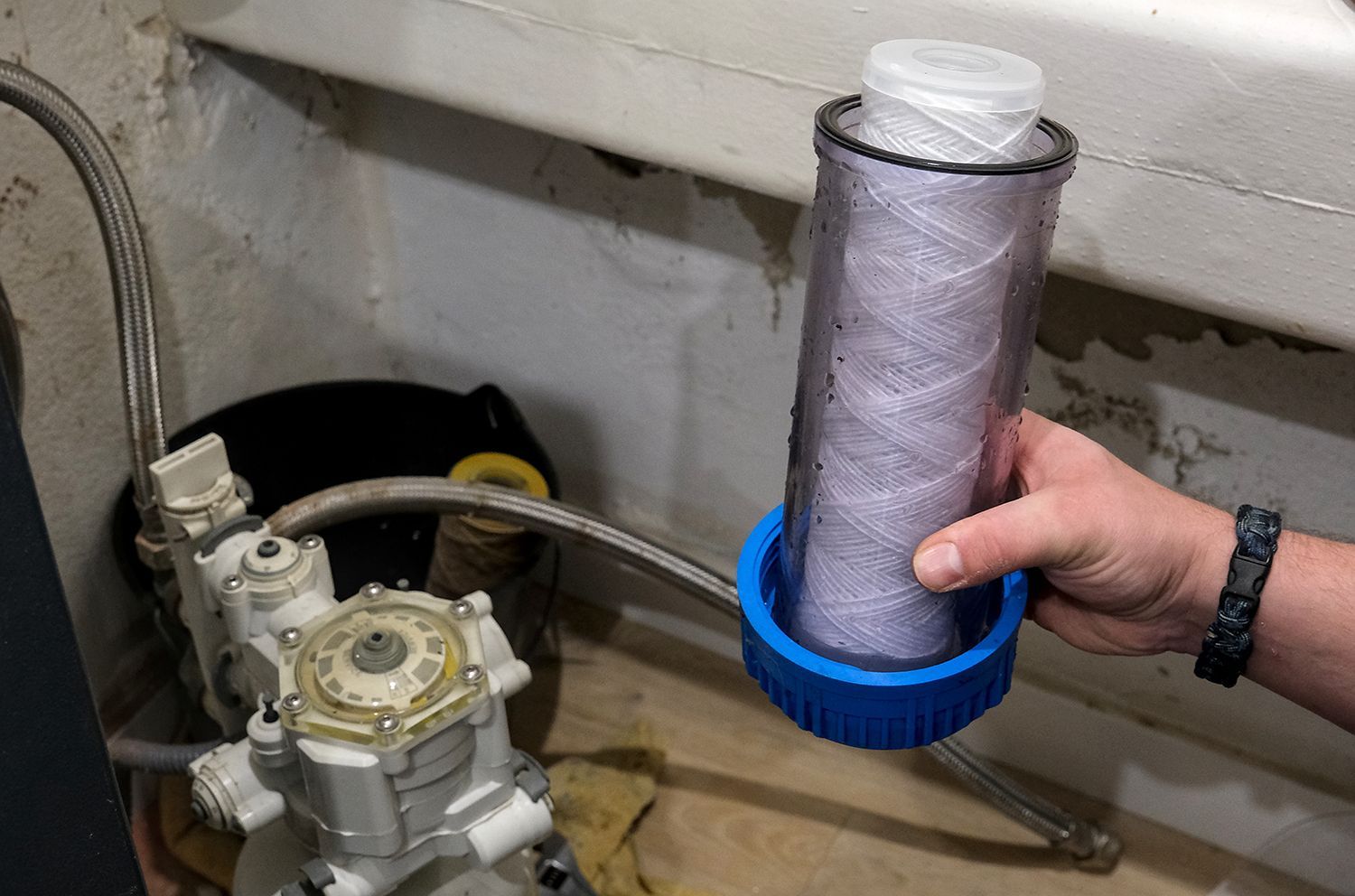 Hand holding a gray filter cartridge with a blue cap beside a machine in a utility room Hand holding a gray filter cartridge with a blue cap beside a machine in a utility room