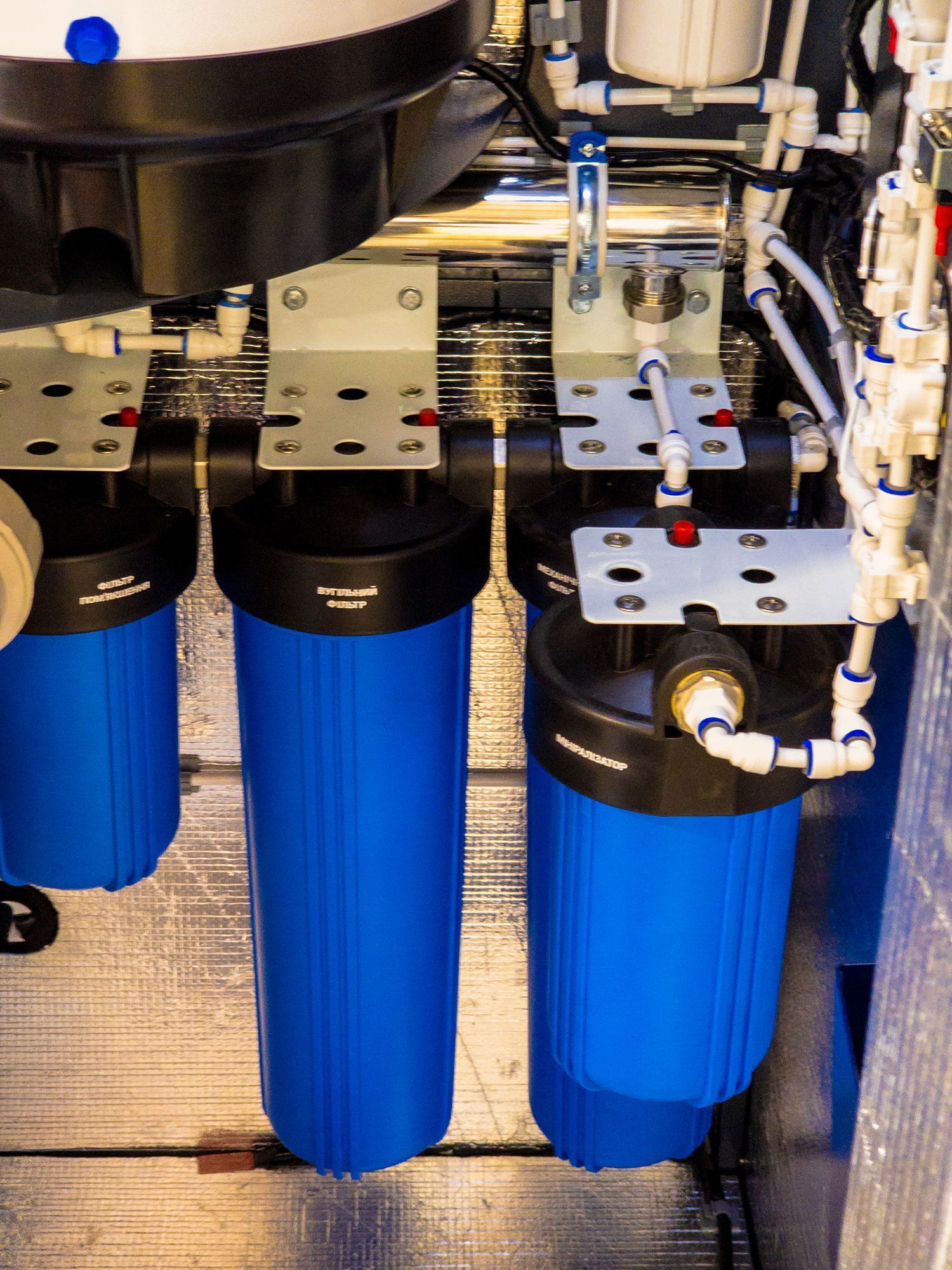 Blue cylindrical water filter system with pipes and valves under a counter Blue cylindrical water filter system with pipes and valves under a counter
