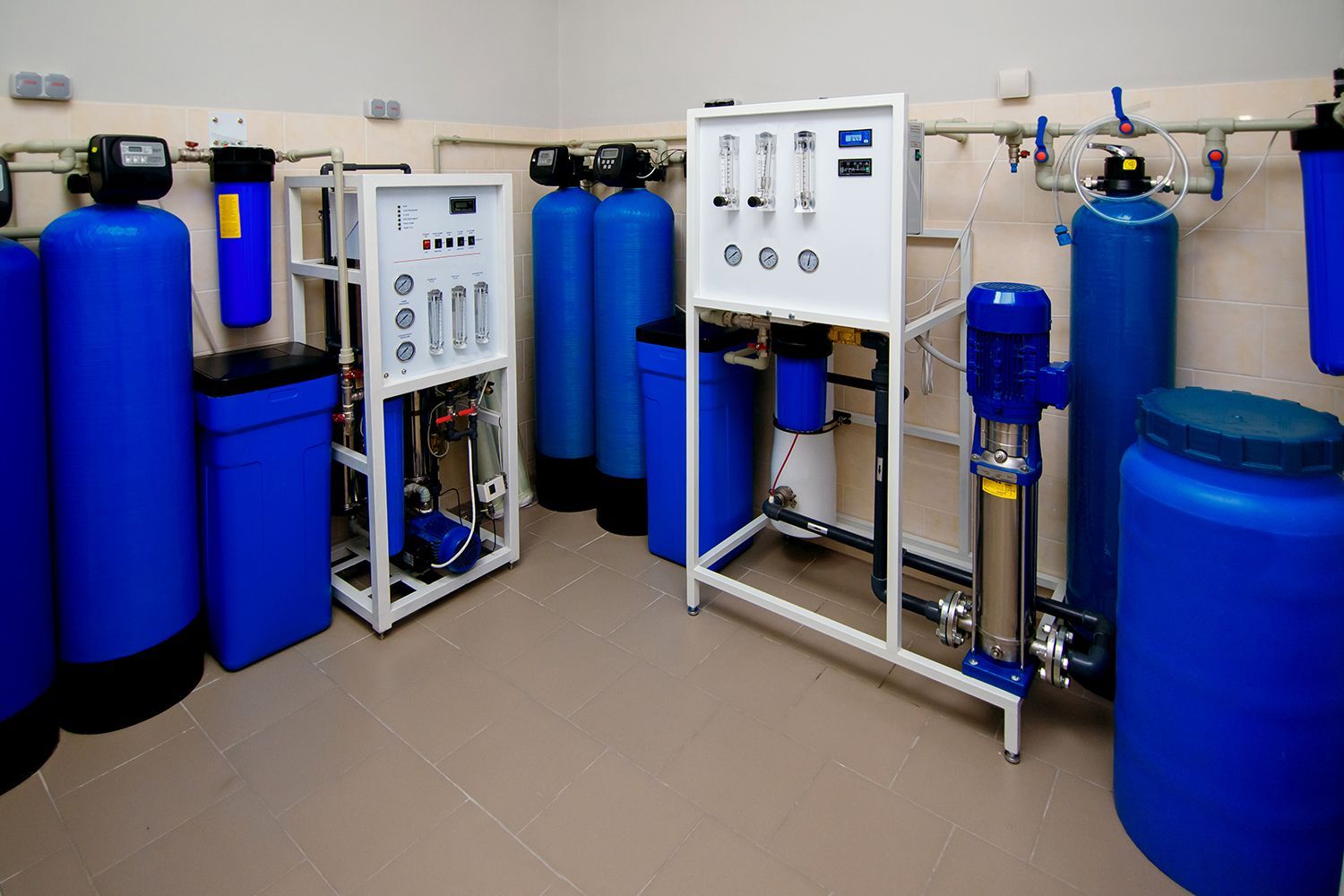 Water treatment room with blue filtration tanks, pipes, and control panels on a tiled floor Water treatment room with blue filtration tanks, pipes, and control panels on a tiled floor