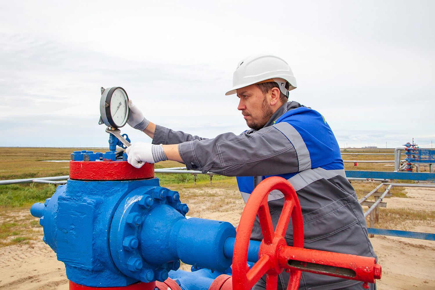 Worker adjusting a blue industrial valve with a red wheel on a pipeline outdoors Worker adjusting a blue industrial valve with a red wheel on a pipeline outdoors