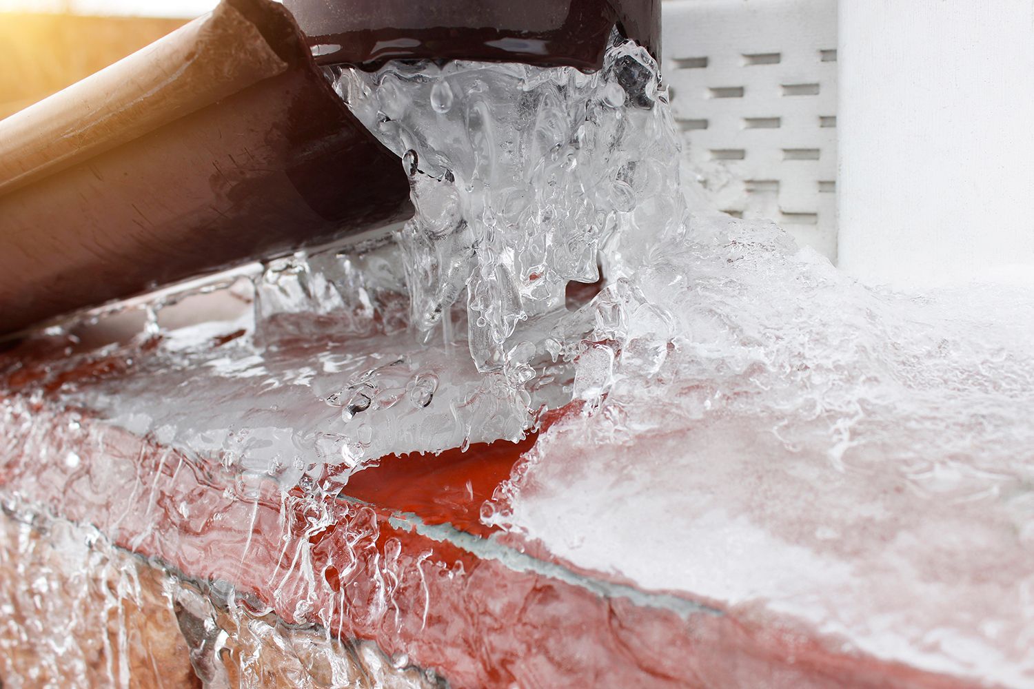Water pouring from a brown pipe onto wet red bricks and splashing over a white perforated surface