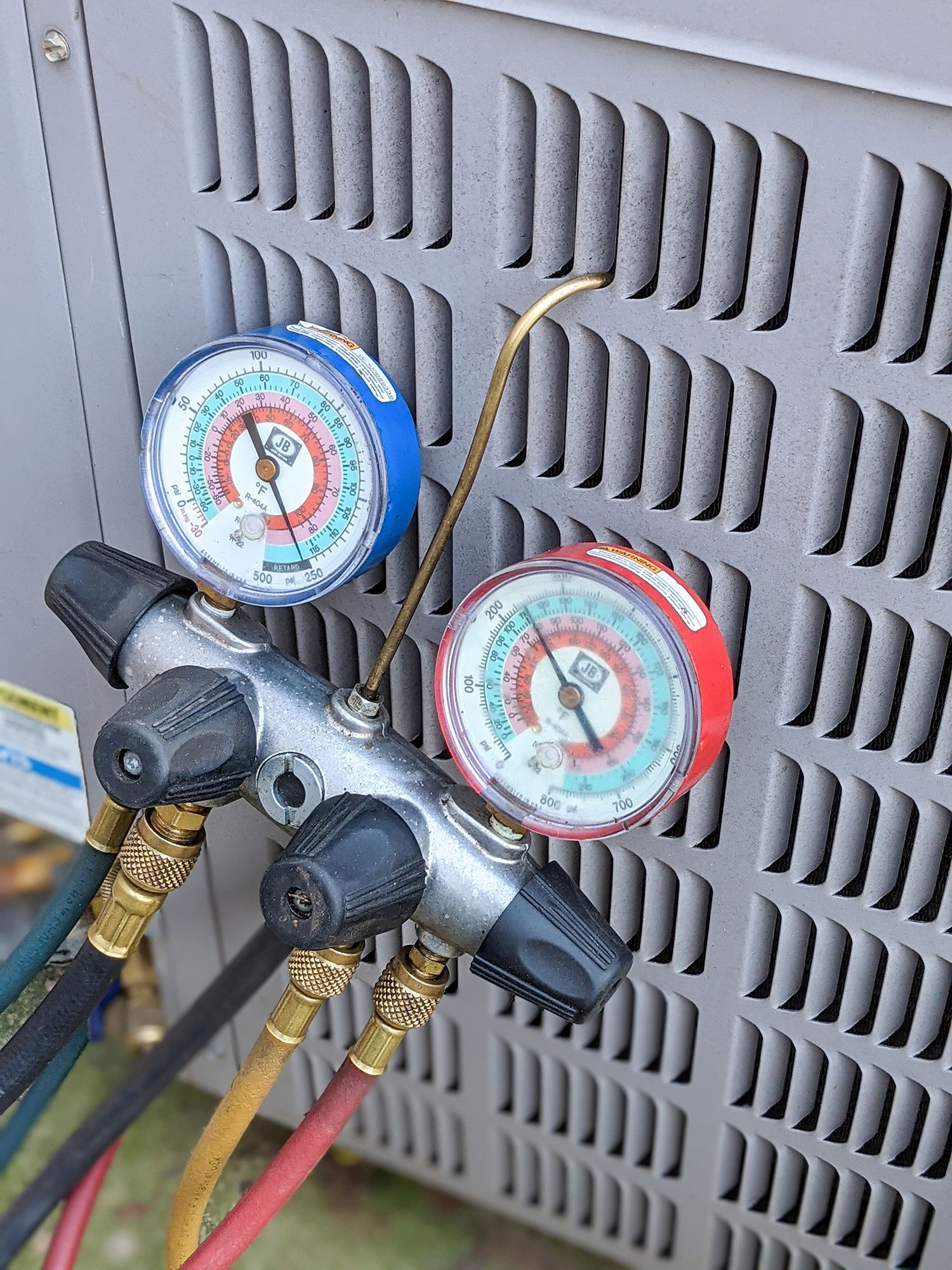 HVAC manifold gauges with red and blue dials connected to hoses on an outdoor unit HVAC manifold gauges with red and blue dials connected to hoses on an outdoor unit