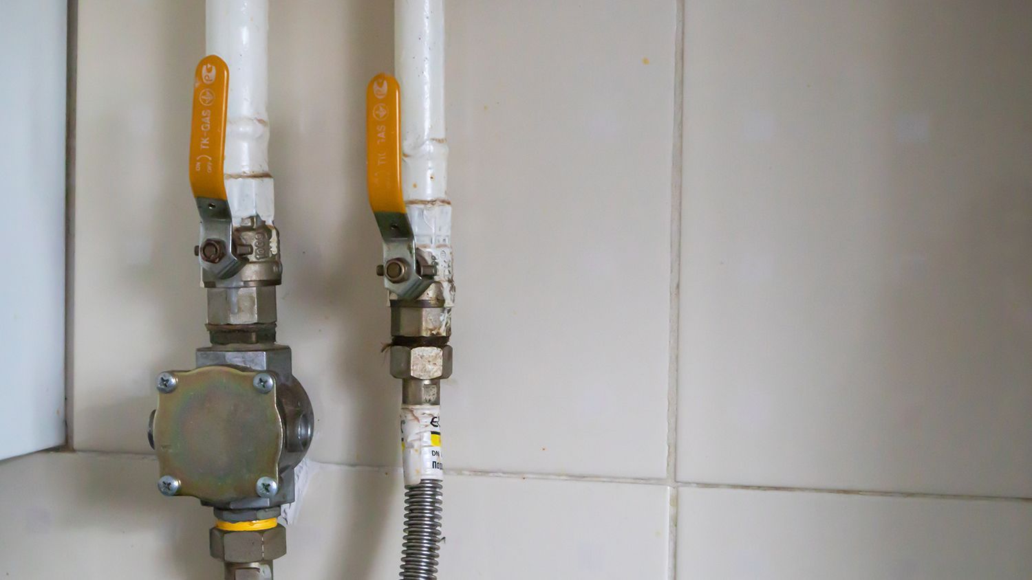 Two yellow-handled gas shutoff valves mounted on a wall, one with a flexible metal hose.