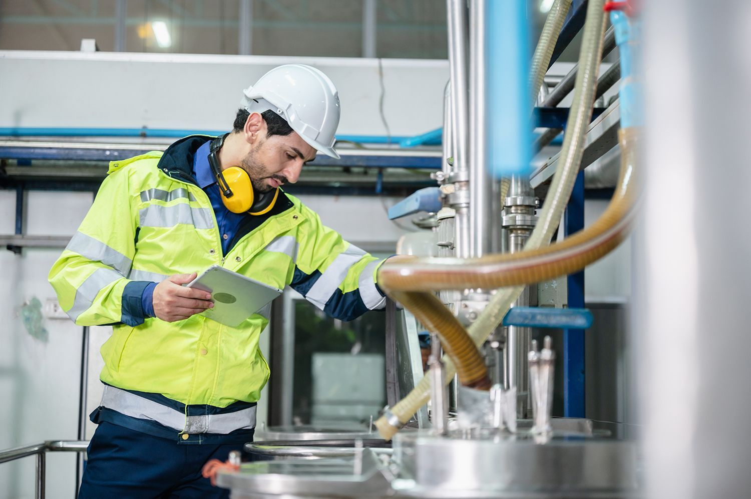 Worker in hard hat and high-vis jacket inspecting industrial machinery with a clipboard Worker in hard hat and high-vis jacket inspecting industrial machinery with a clipboard