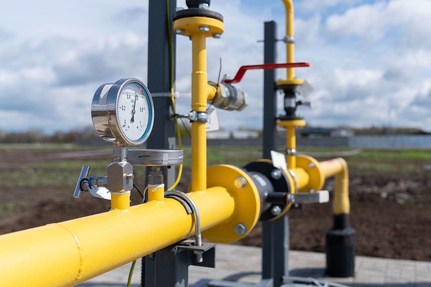 Yellow gas pipeline with pressure gauges and valves in an outdoor industrial field