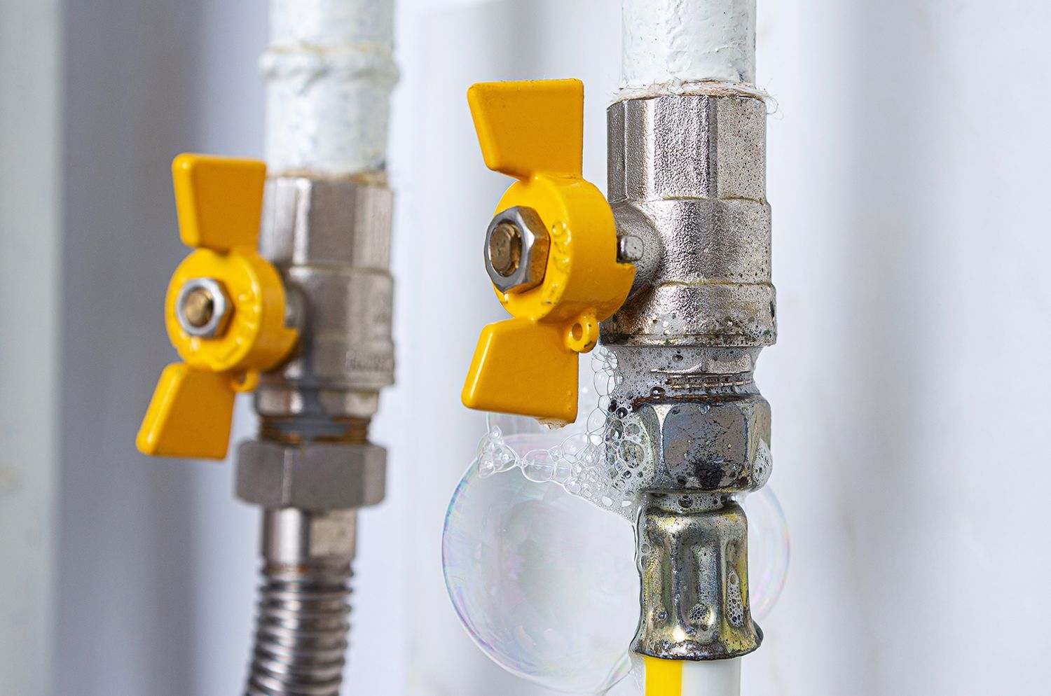Two yellow water shutoff valves on silver pipes, one with a hanging droplet