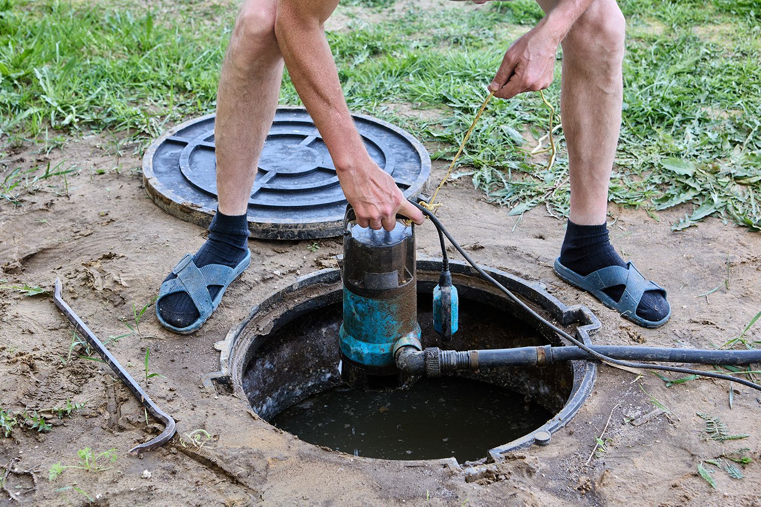 Person using a hand pump over an open well in a grassy yard Person using a hand pump over an open well in a grassy yard