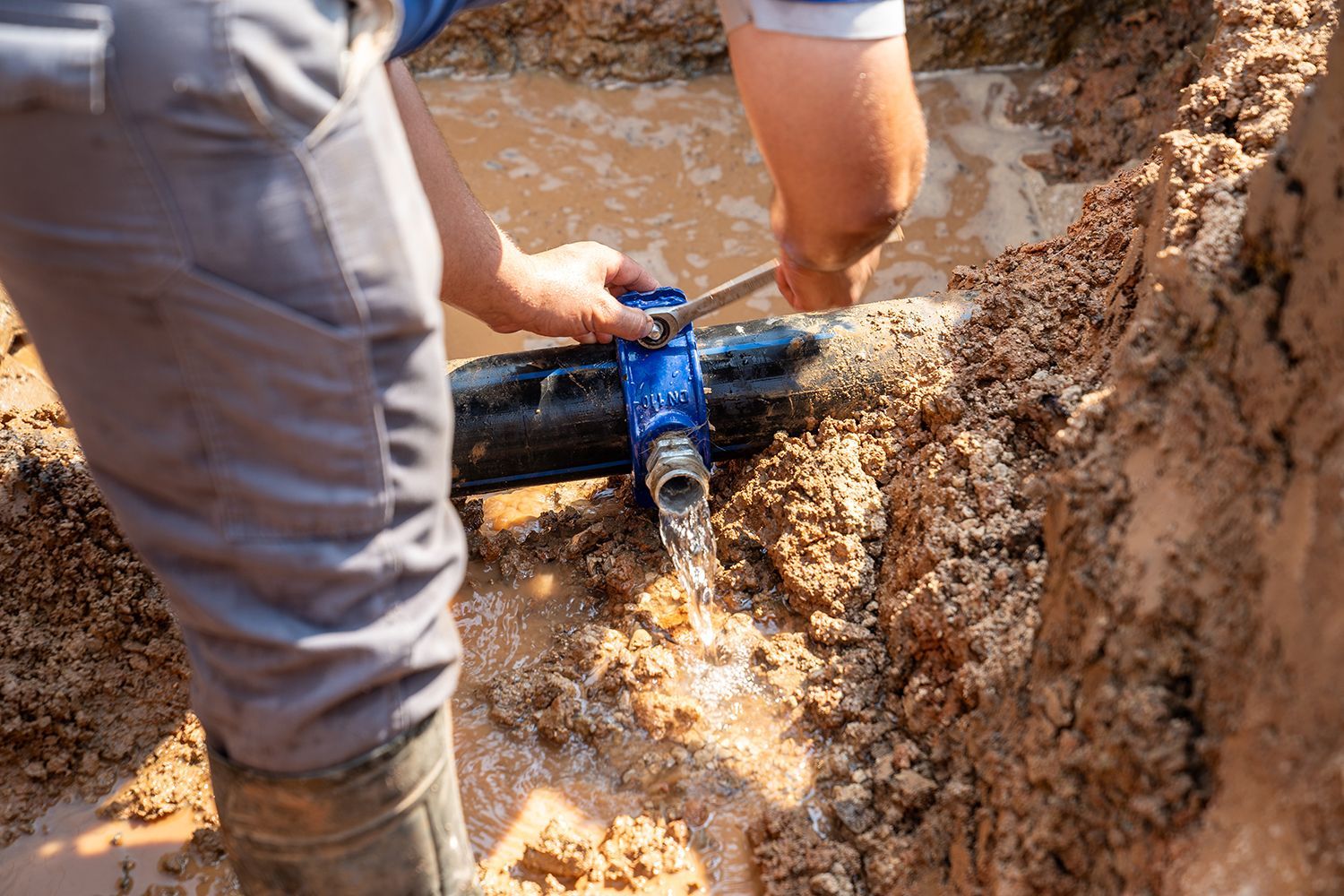 Worker repairing a black water pipe in muddy soil, water spraying from the leak Worker repairing a black water pipe in muddy soil, water spraying from the leak