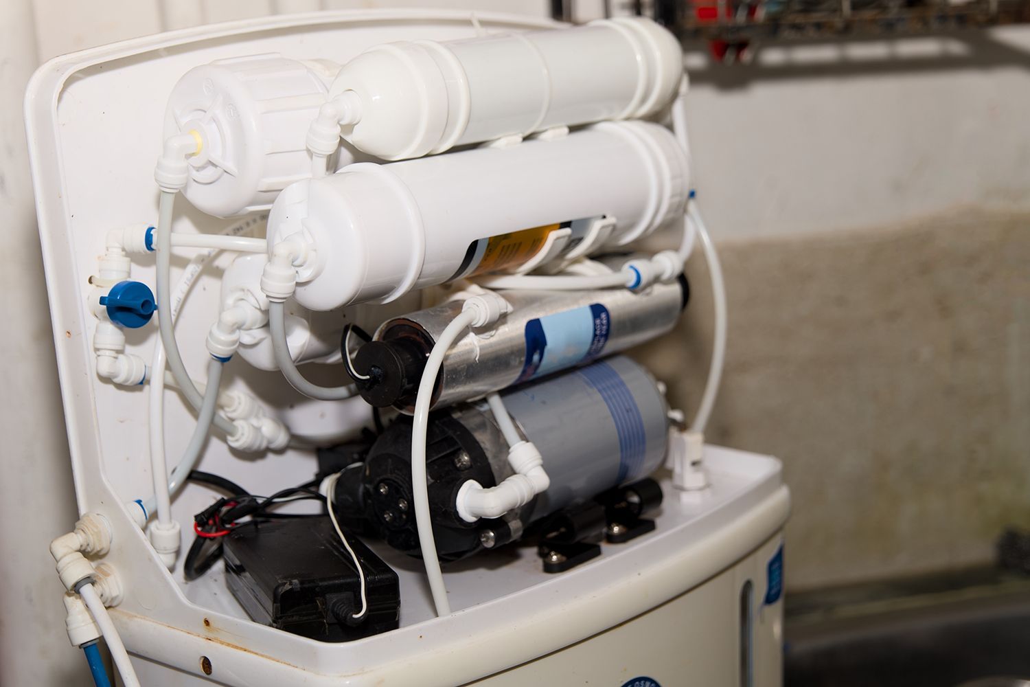 Under-sink water filtration system with white and blue components and tubing in a cabinet Under-sink water filtration system with white and blue components and tubing in a cabinet