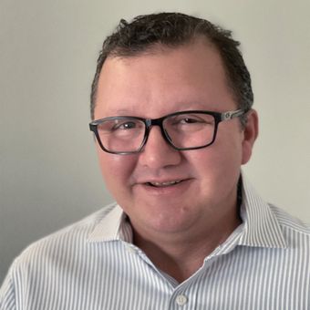 A man wearing glasses and a striped shirt is smiling for the camera.