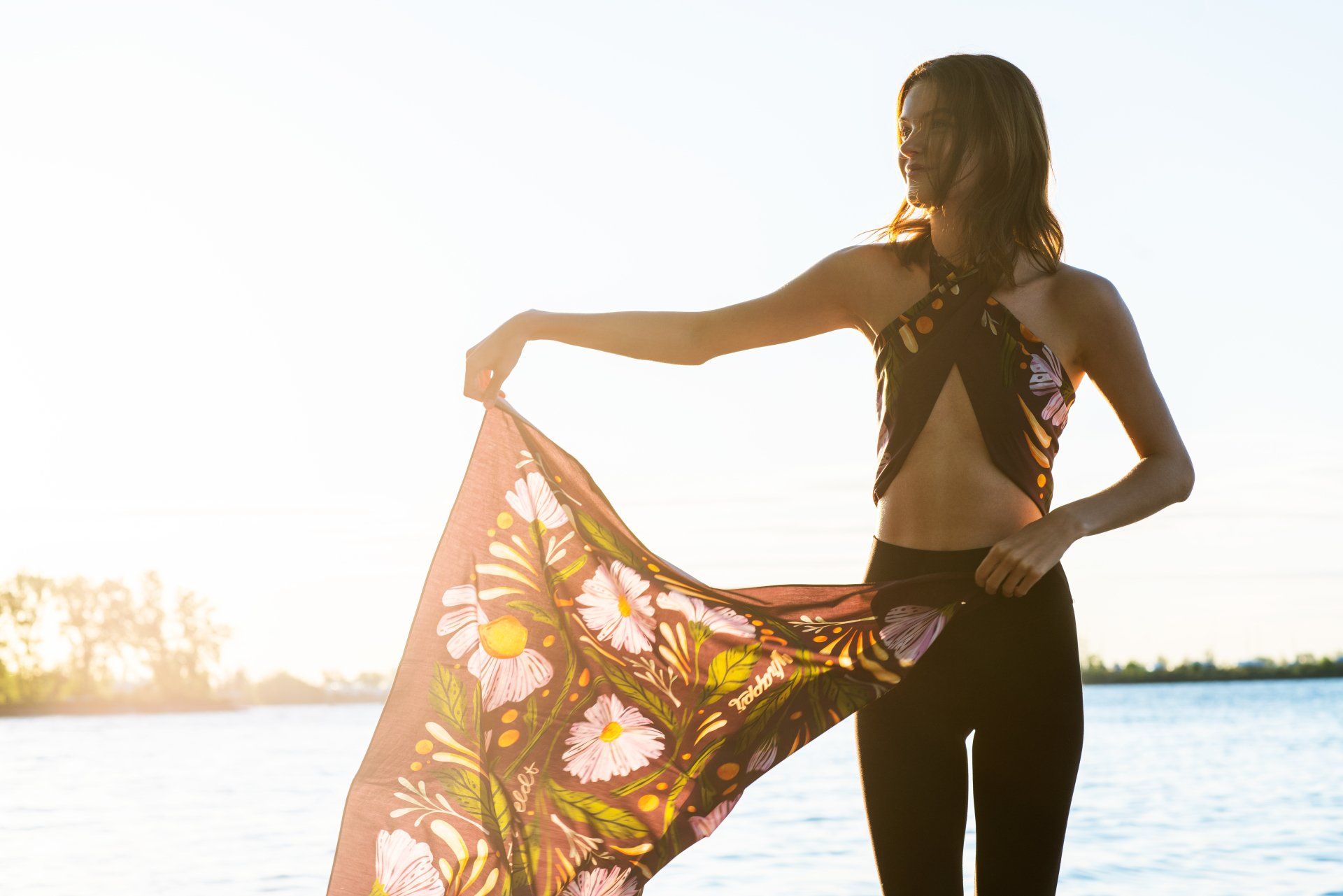 a woman is standing on the beach holding a scarf around her neck .